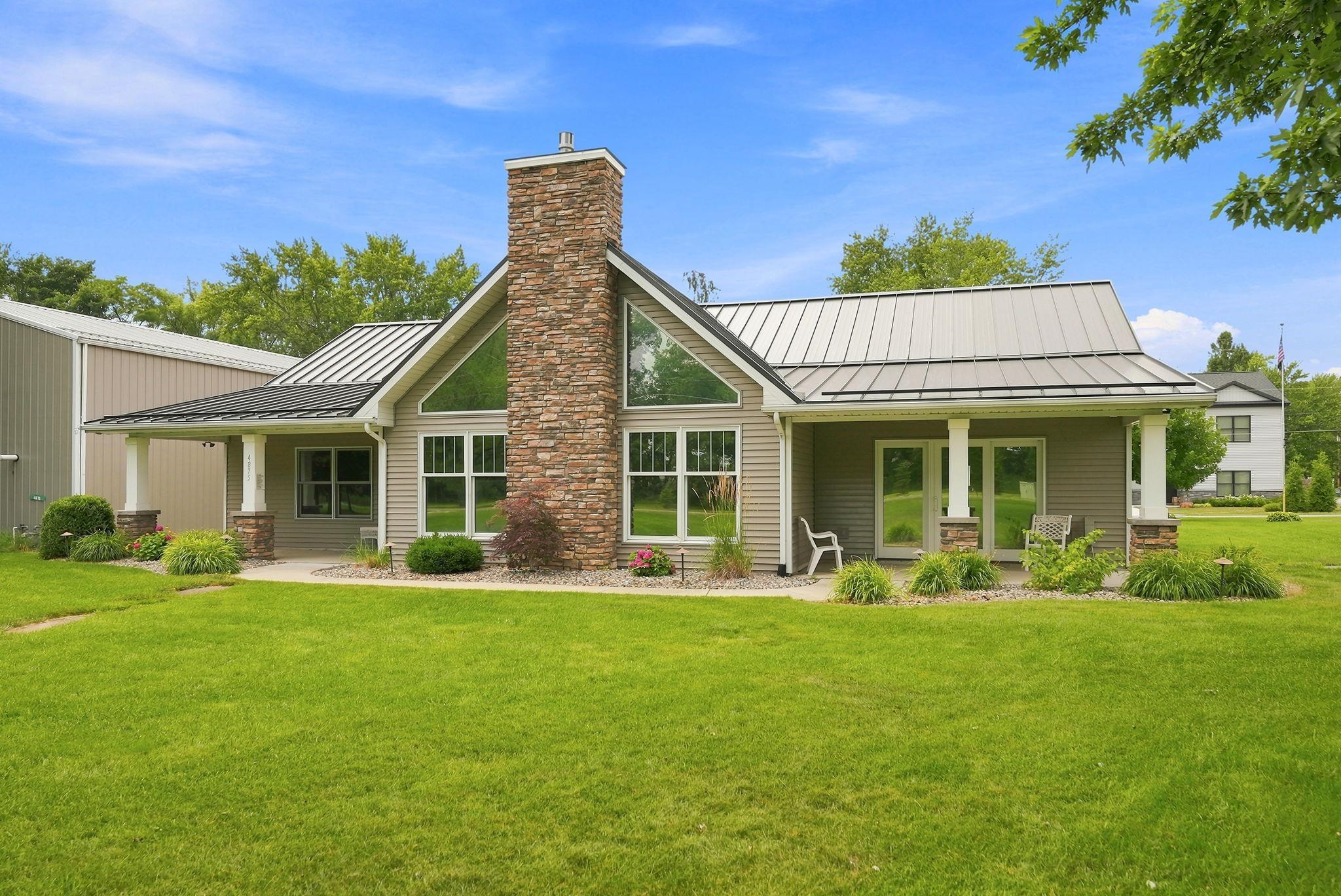 Image 3: Contemporary-style exterior featuring a stone chimney, extensive window-pane detailing, a metal roof, and a covered porch with stone-wrapped columns, Back Of Structure Image 3: Contemporary-style exterior featuring a stone chimney, extensive window-pane detailing, a metal roof, and a covered porch with stone-wrapped columns, Back Of Structure