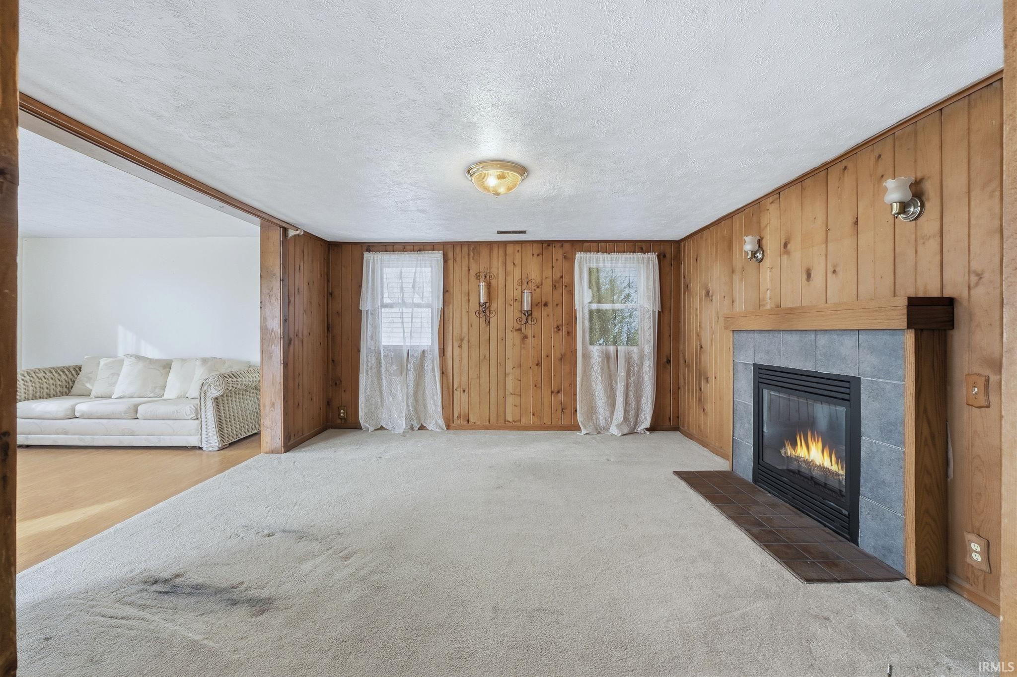 Image 1: Unfurnished living room featuring wooden walls, a tiled fireplace, a textured ceiling, and carpet floors, Living Room