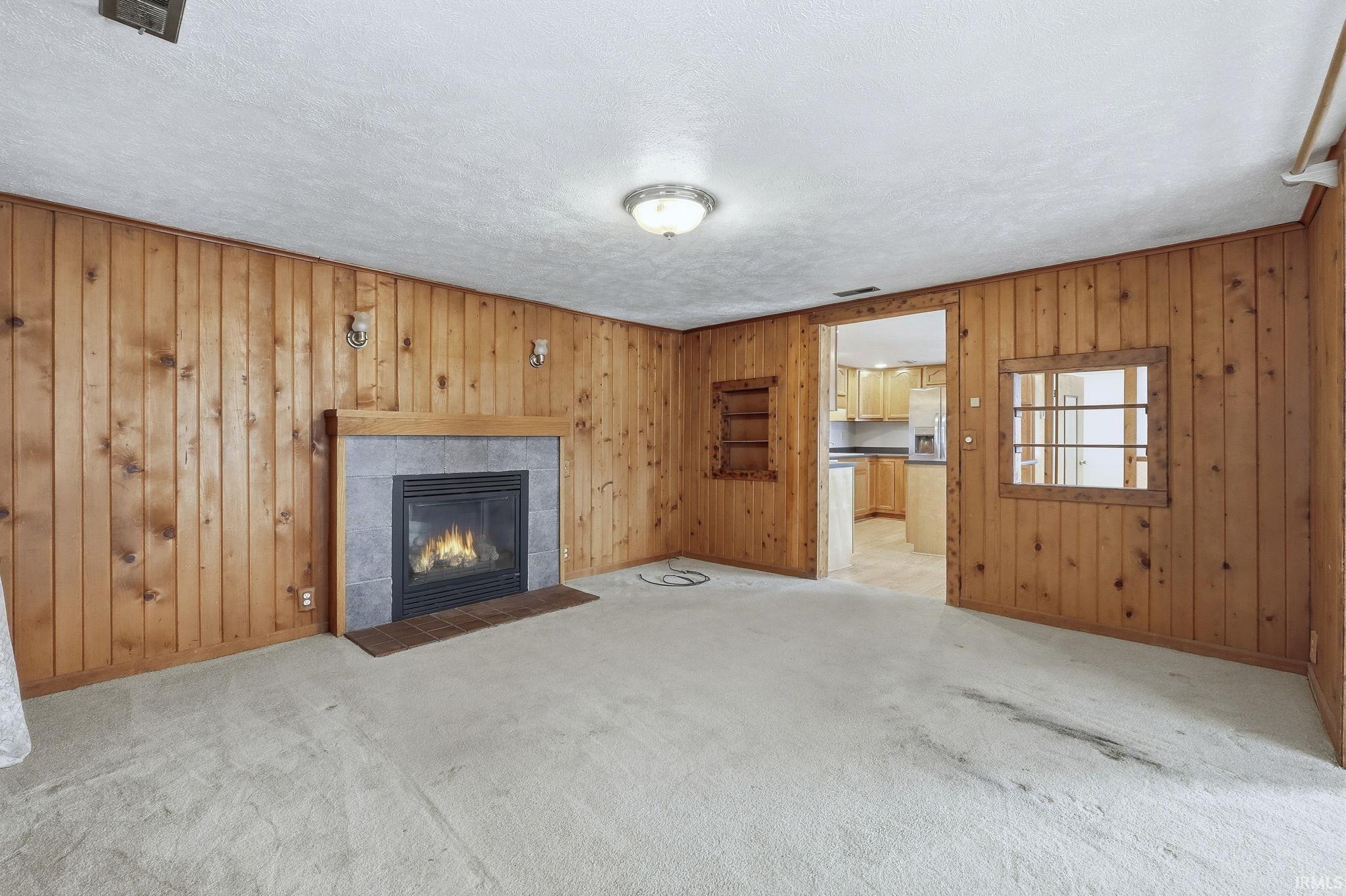 Image 3: Unfurnished living room with wood walls, a textured ceiling, a tiled fireplace, light carpet, and ornamental molding, Living Room
