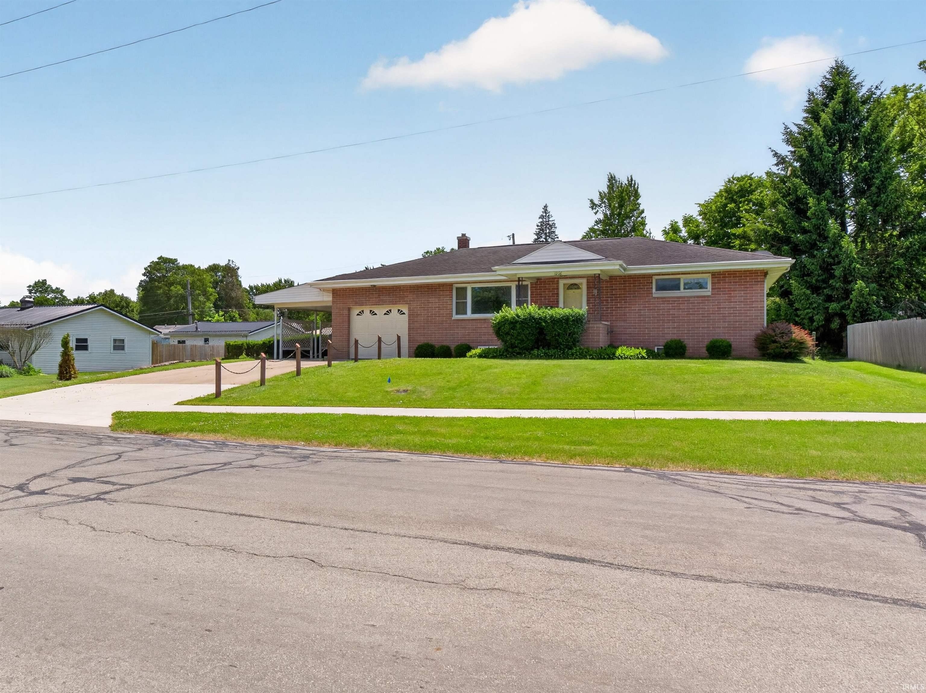 Image 1: Brick exterior residence with a covered carport, attached garage, and an established lawn, Front Of Structure