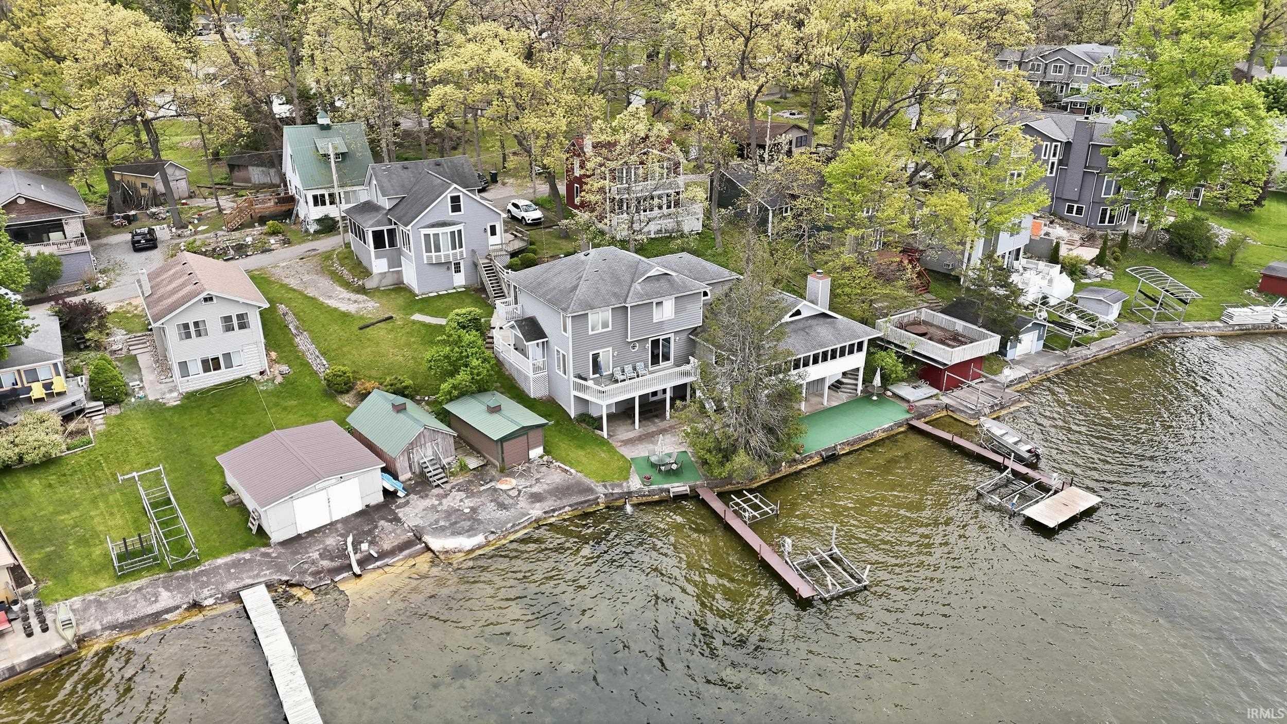 Image 2: Waterfront property featuring a multi-story residence with a rear deck, multiple boat docks, a boathouse, and additional storage sheds, Aerial View