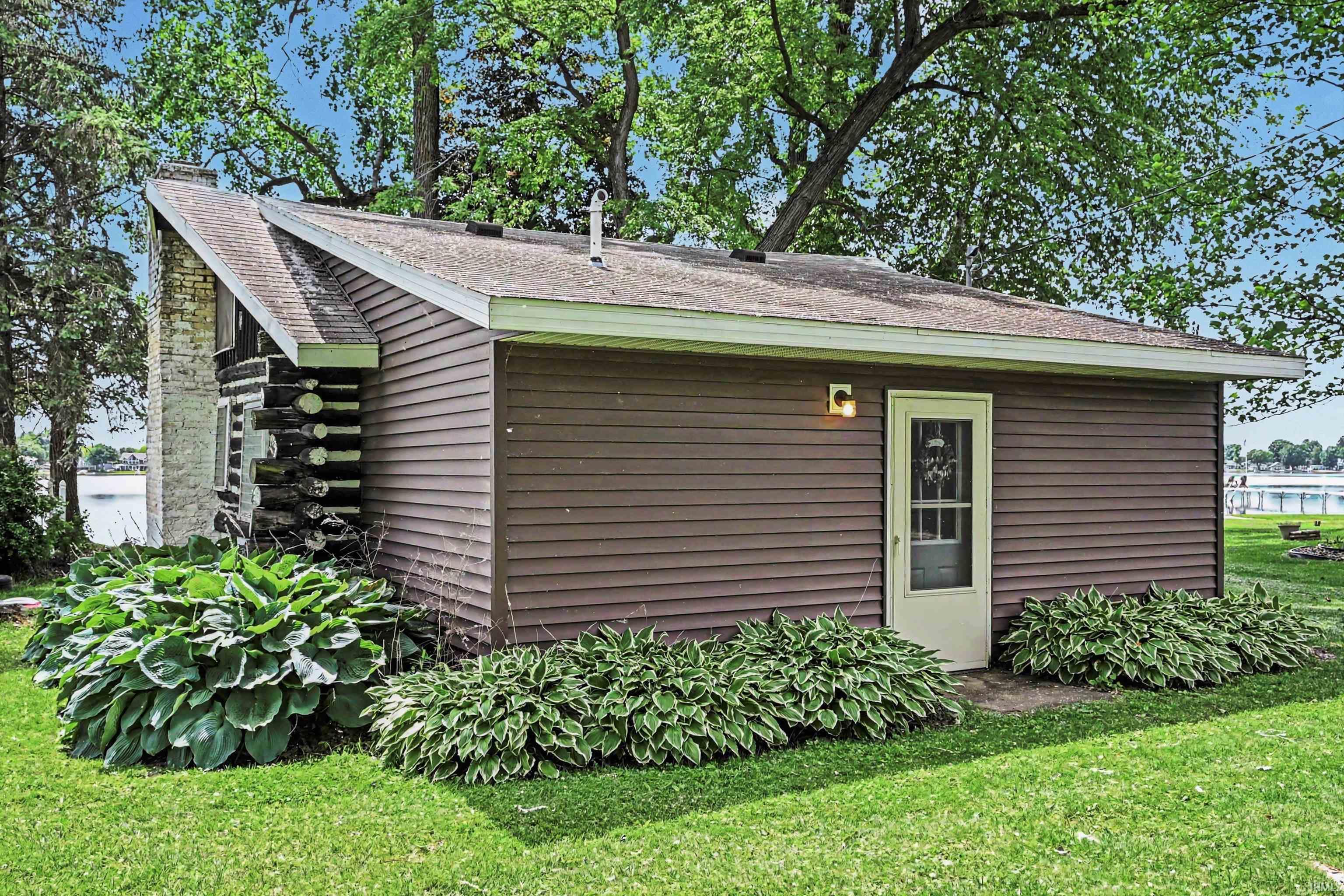 Image 0: Brown horizontal siding structure featuring a white entry door with glass paneling, a brick chimney, and log cabin wall detailing, Out Buildings Image 0: Brown horizontal siding structure featuring a white entry door with glass paneling, a brick chimney, and log cabin wall detailing, Out Buildings
