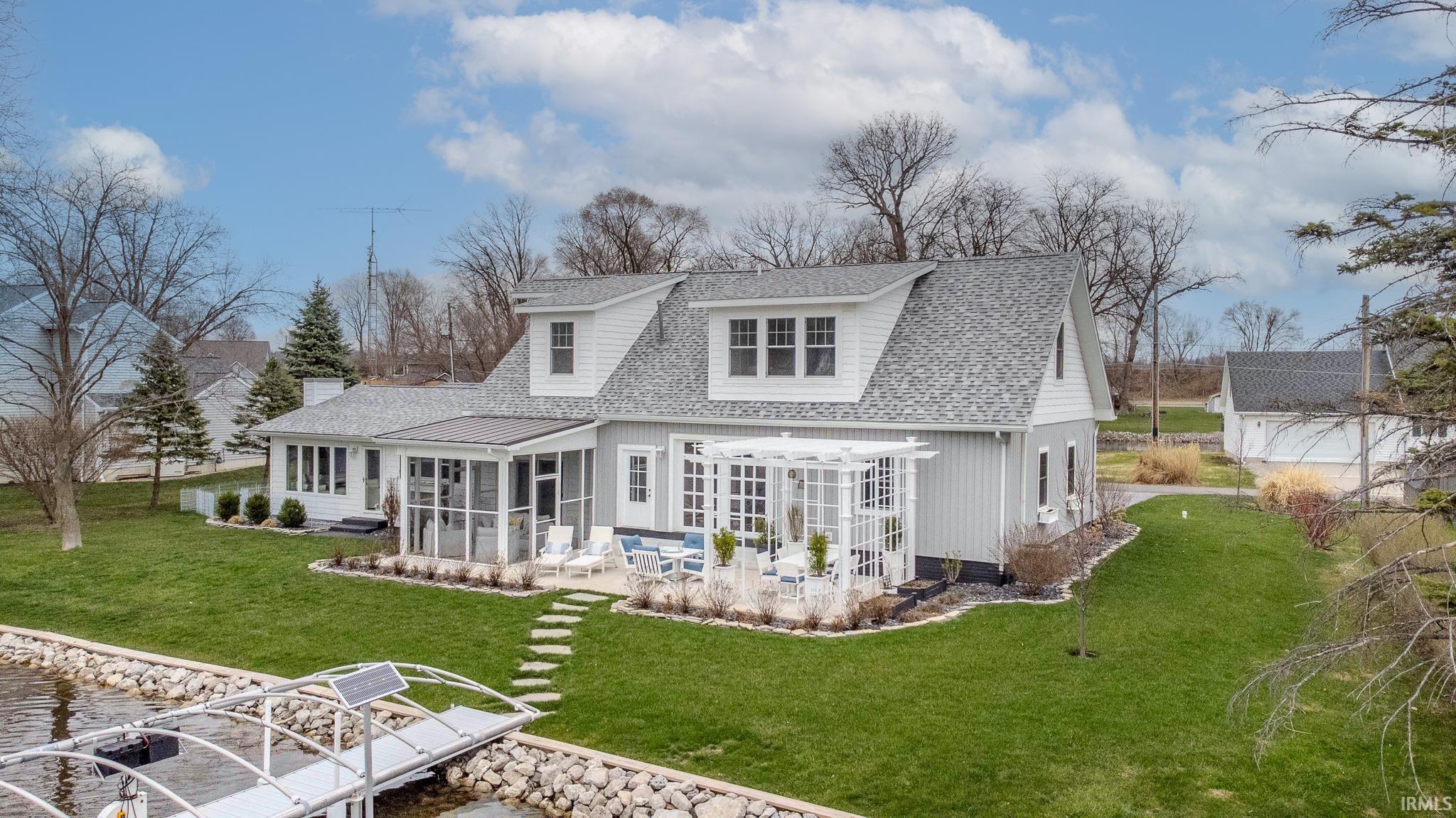 Image 2: Back of property featuring a sunroom, roof with shingles, a lawn, a patio area, and a water view, Back Of Structure Image 2: Back of property featuring a sunroom, roof with shingles, a lawn, a patio area, and a water view, Back Of Structure