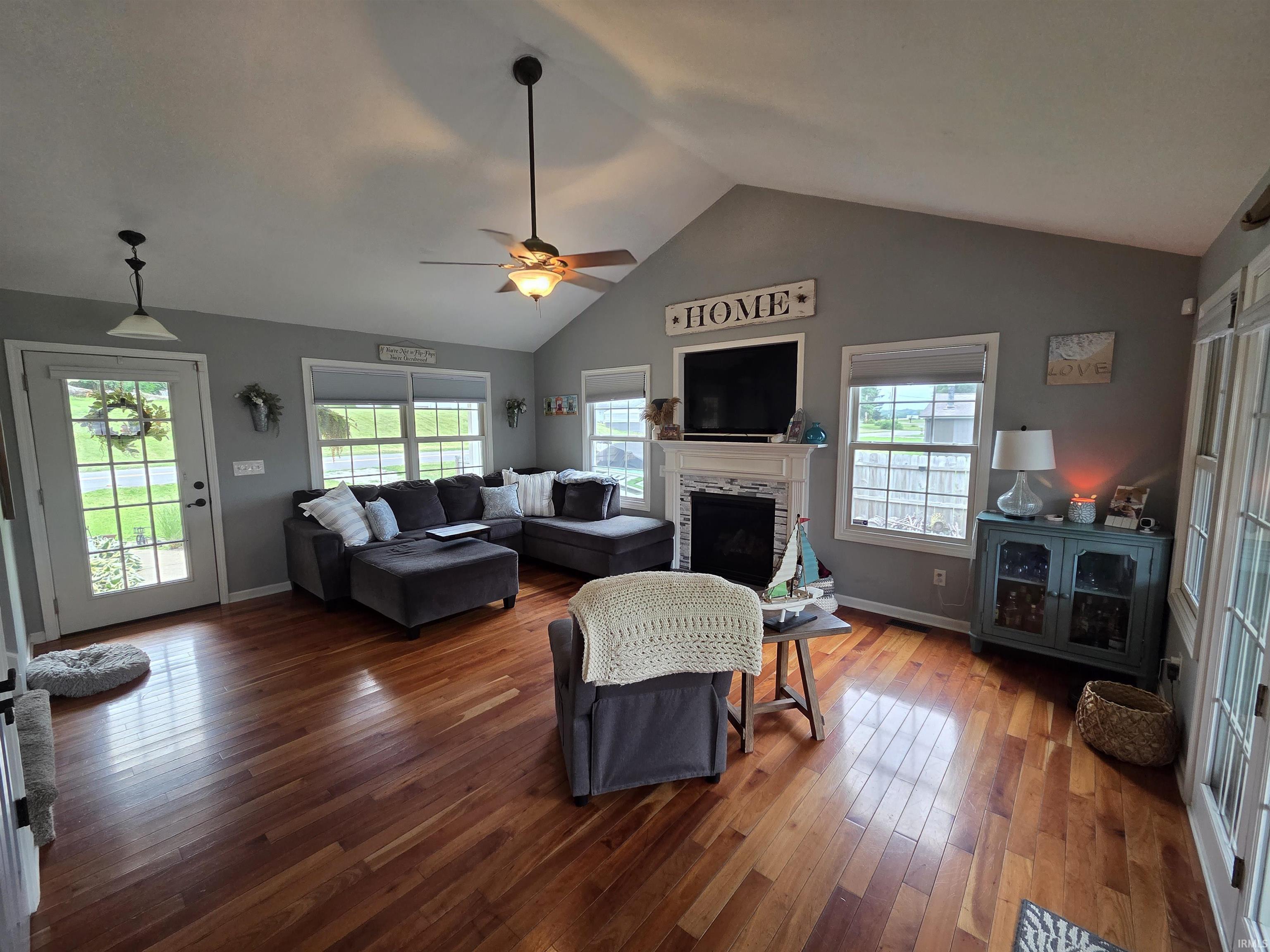 Image 3: Living area featuring wood-finish flooring, vaulted ceilings, and a white fireplace mantel with a tiled surround, Living Room