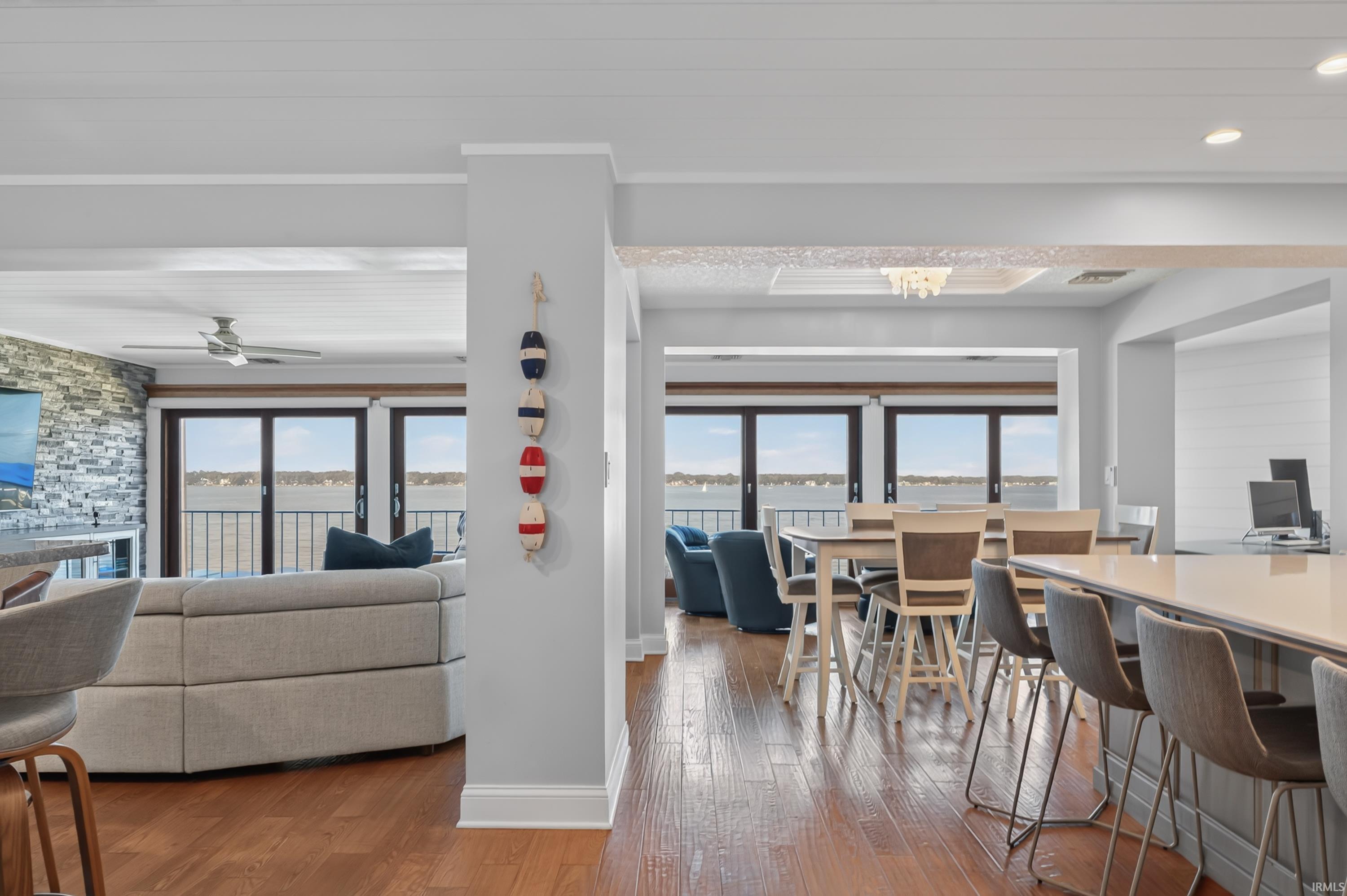 Image 1: Open-concept living space featuring wood-finish flooring, a stacked stone accent wall, and multiple glass doors leading to a waterfront balcony, Dining Area