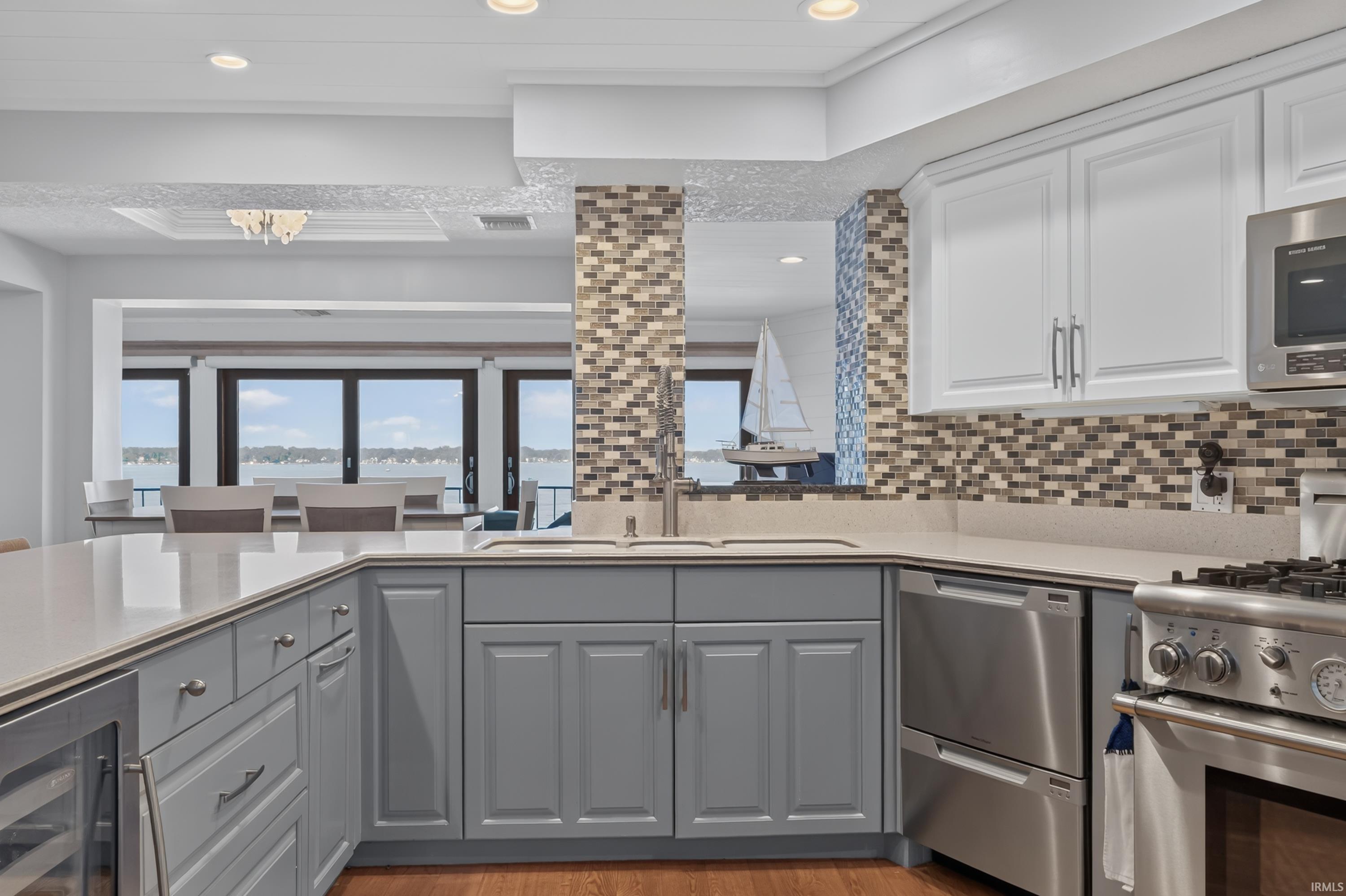 Image 3: Kitchen featuring two-tone cabinetry with light grey base cabinets and white upper cabinets, stainless steel appliances, mosaic tile backsplash, and light-toned countertops, Kitchen