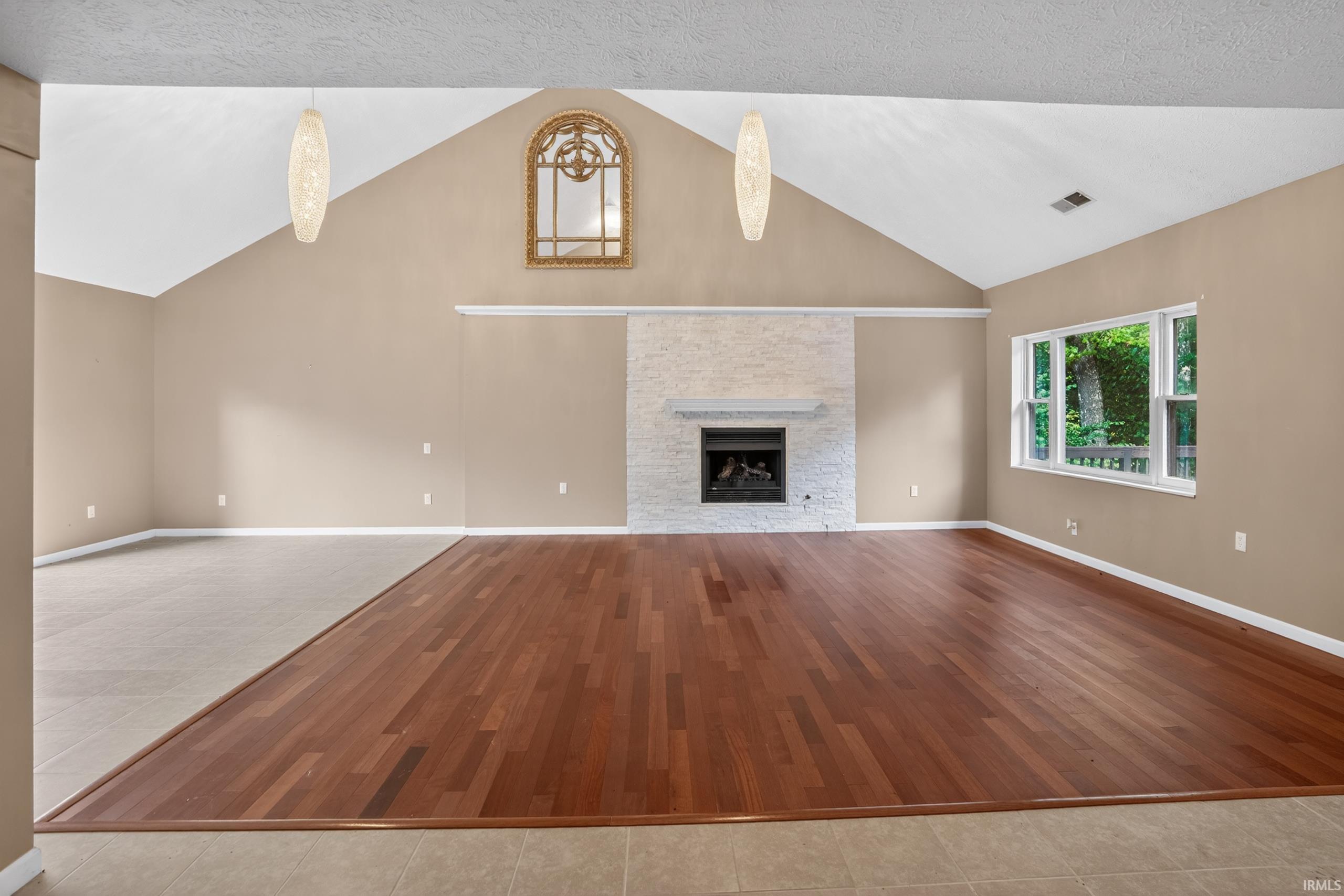 Image 1: Vaulted ceiling great room featuring a tiled fireplace with mantel, rich wood-finish flooring, and a large bay window, Living Room