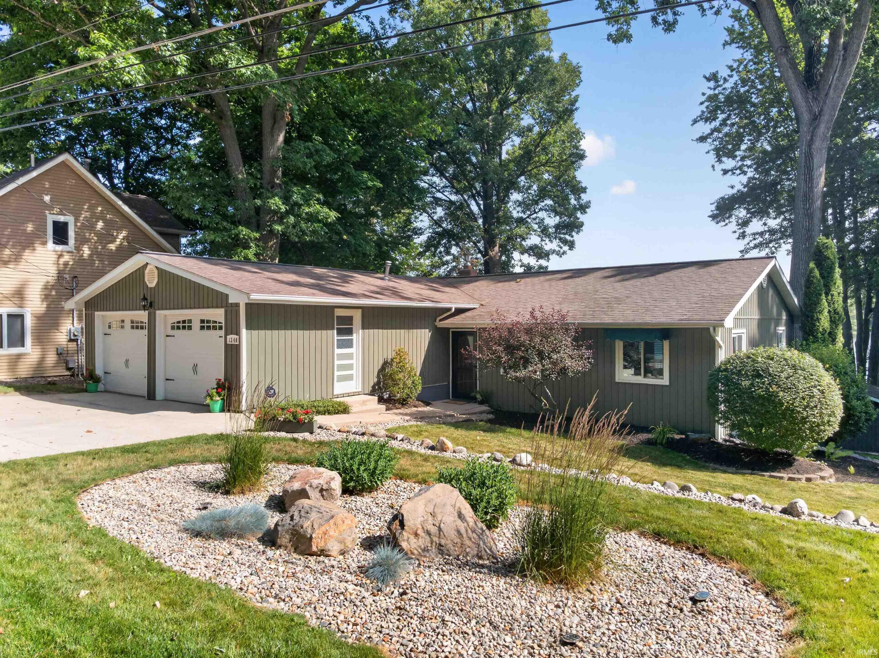Image 0: Ranch-style residence featuring green vertical siding, a two-car garage with white paneled doors, and a concrete driveway, Front Of Structure Image 0: Ranch-style residence featuring green vertical siding, a two-car garage with white paneled doors, and a concrete driveway, Front Of Structure