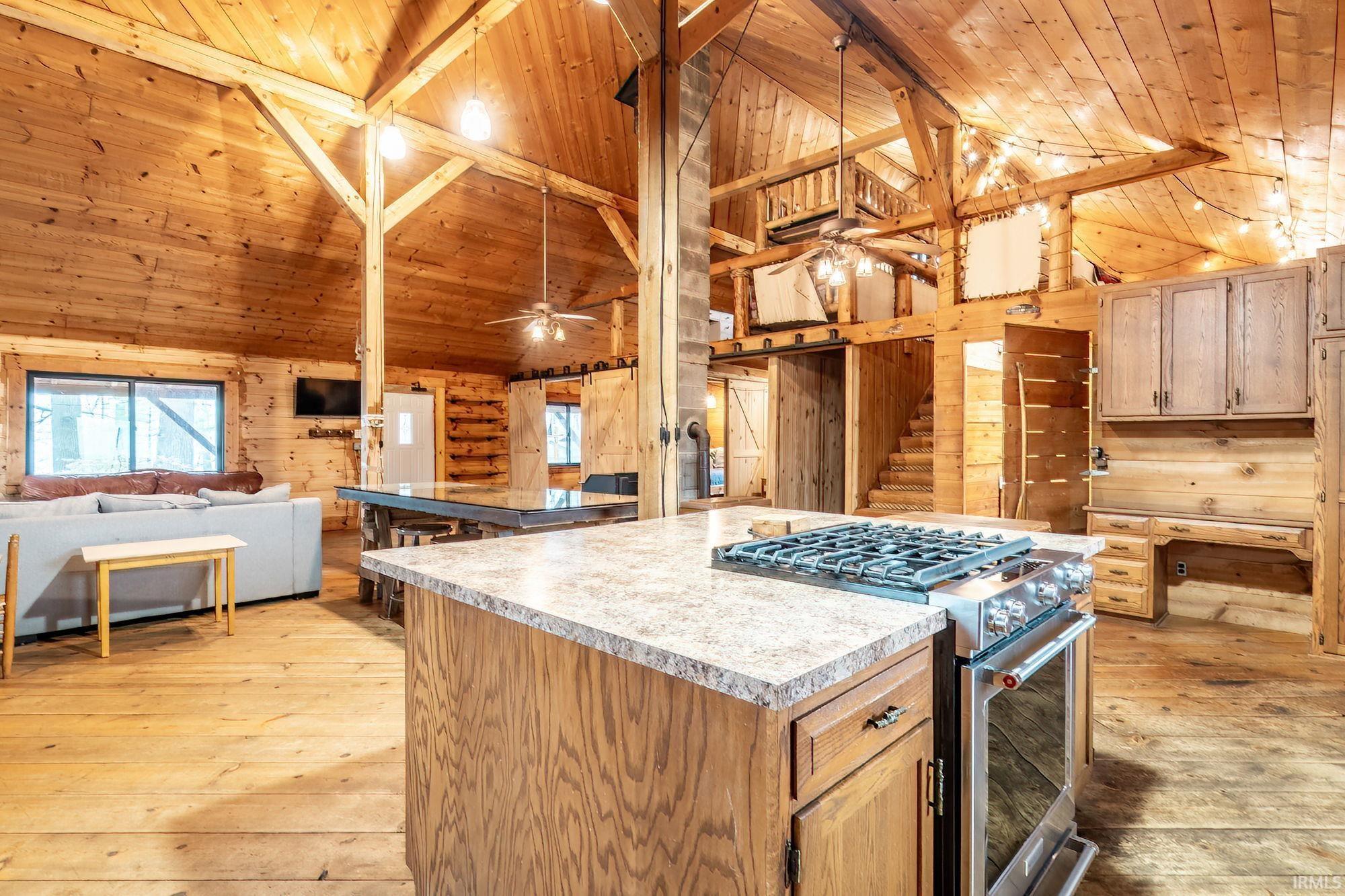 Image 3: Kitchen with light wood-type flooring, a high wood beamed ceiling, stainless steel gas stove, wood walls, and open floor plan, Kitchen Image 3: Kitchen with light wood-type flooring, a high wood beamed ceiling, stainless steel gas stove, wood walls, and open floor plan, Kitchen