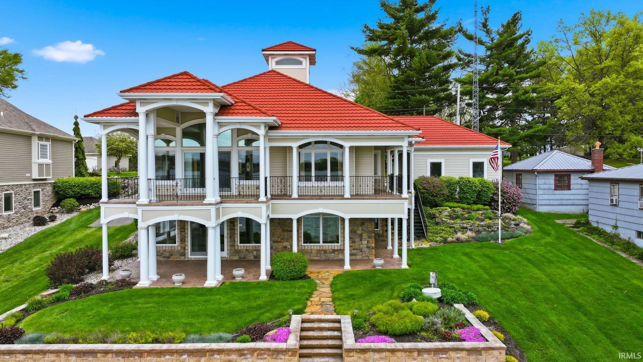 Image 0: Multi-level residence featuring a red tile roof, expansive balconies with decorative railings, and a stone-clad lower level, Back Of Structure