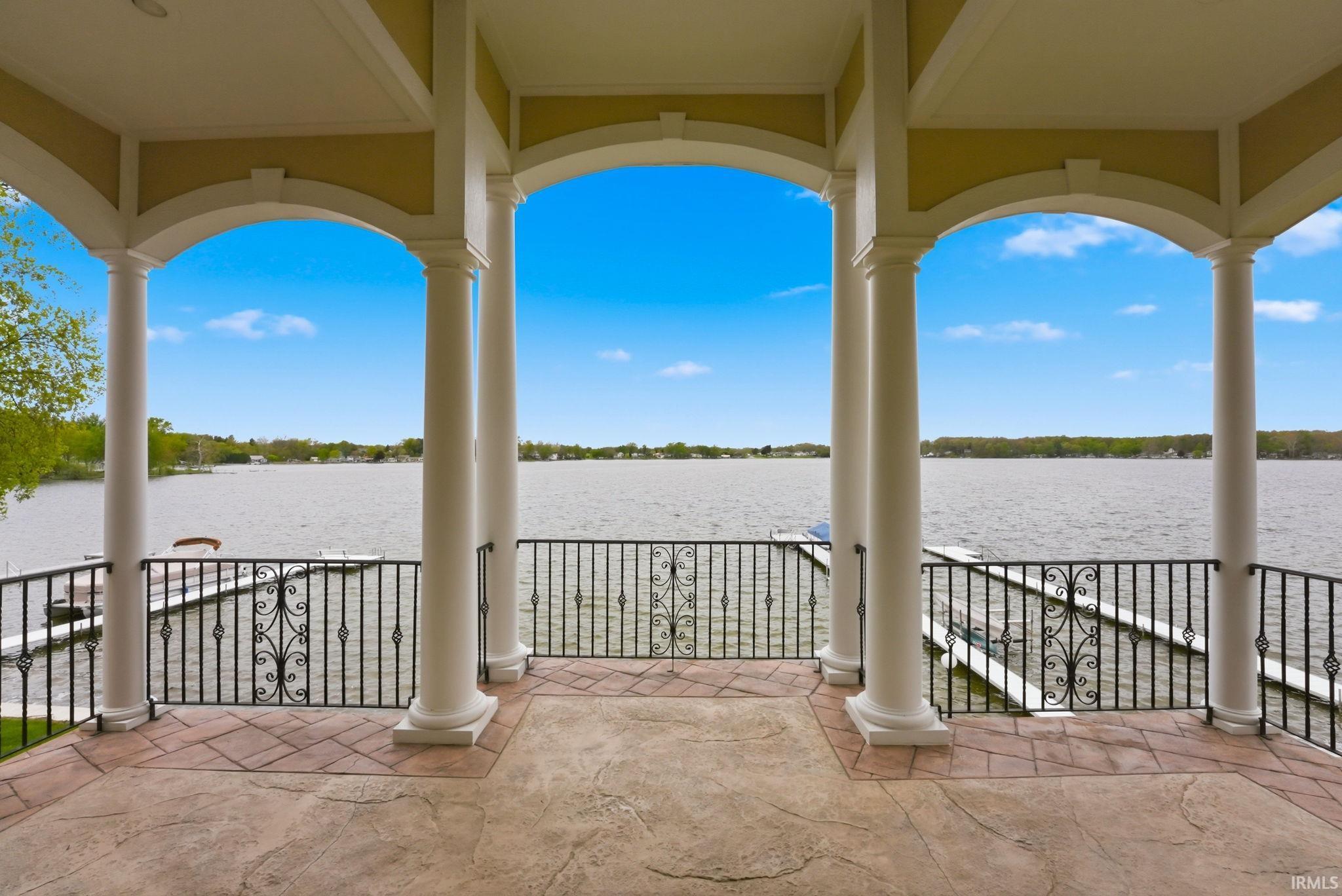 Image 1: Waterfront covered patio featuring classical columns, arched openings, wrought iron railings, and a stamped concrete floor, Patio