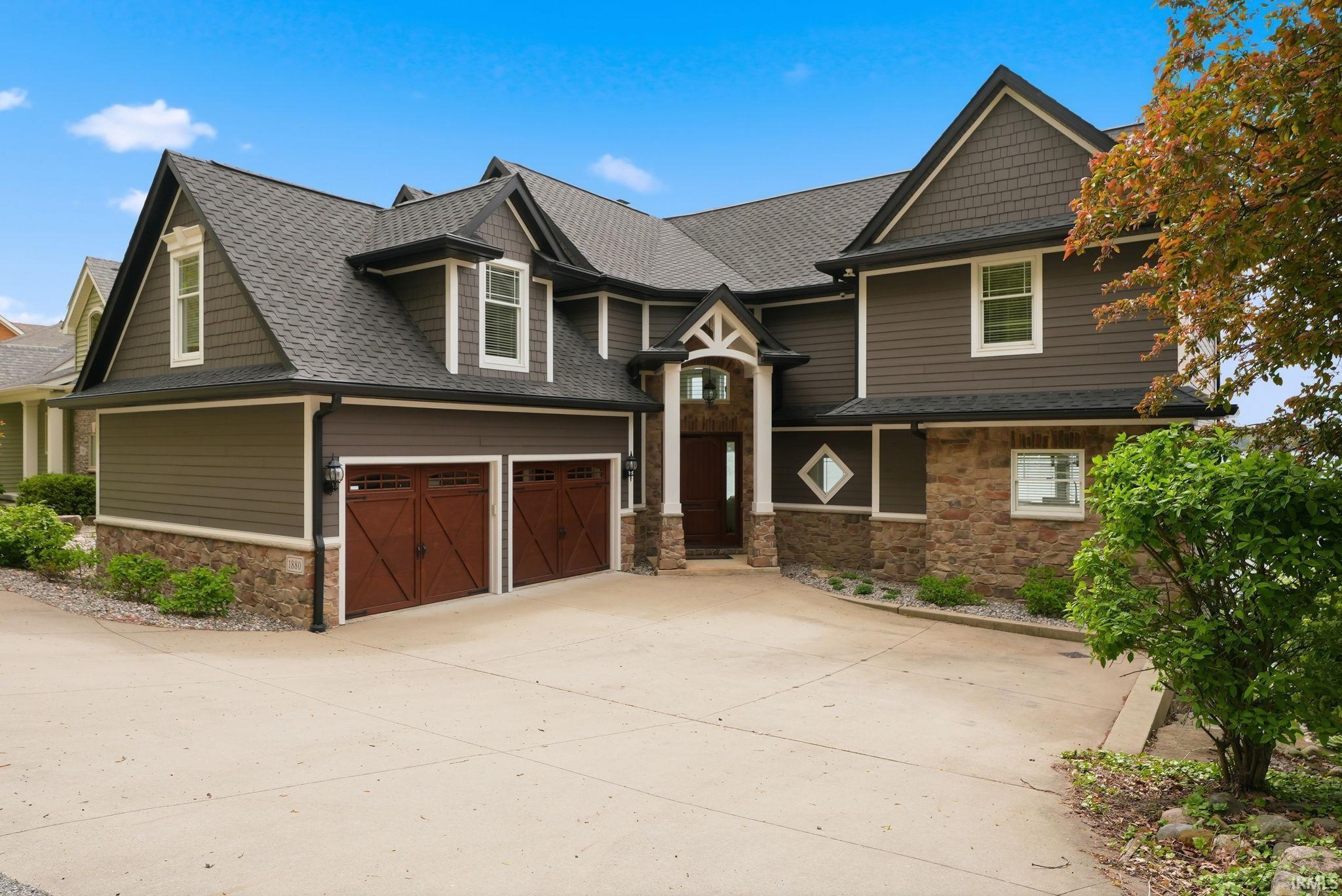 Image 1: Multi-level residence featuring dark siding, stone accents, a dark shingle roof, and a prominent two-car garage with wood-finish doors, Front Of Structure Image 1: Multi-level residence featuring dark siding, stone accents, a dark shingle roof, and a prominent two-car garage with wood-finish doors, Front Of Structure