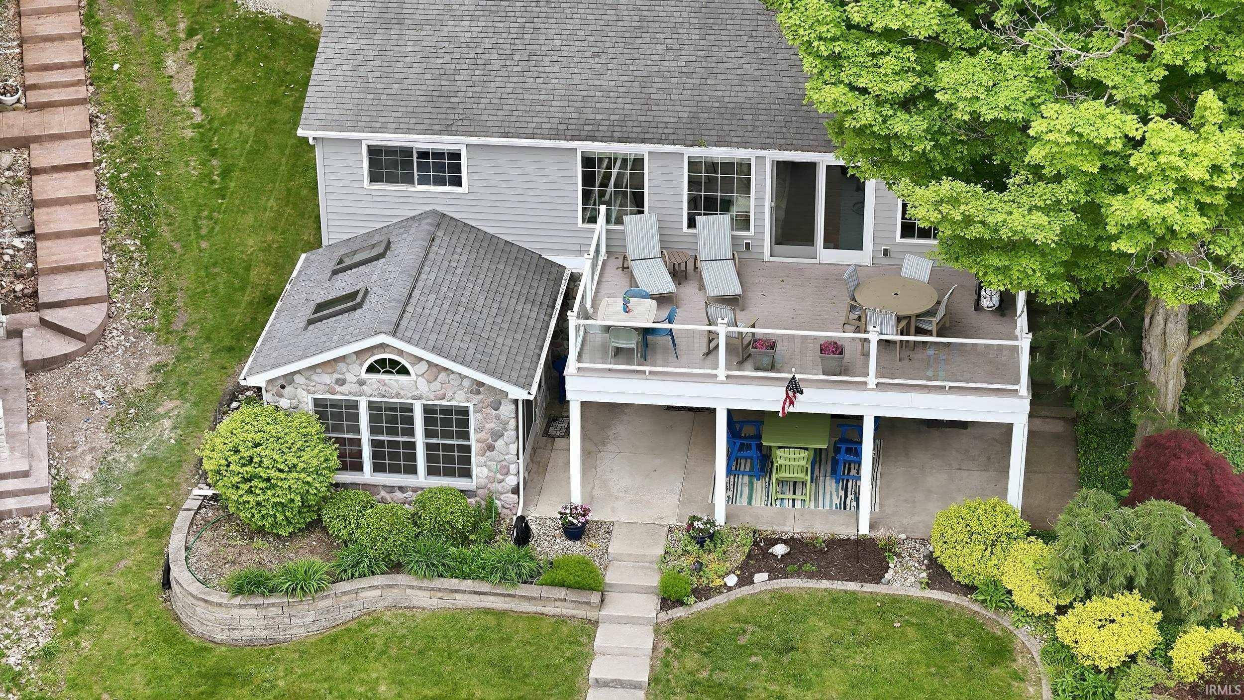 Image 1: Multi-level property featuring a stone and siding exterior with a shingled roof, an upper-level deck with glass railing, and a lower-level covered patio, Aerial View