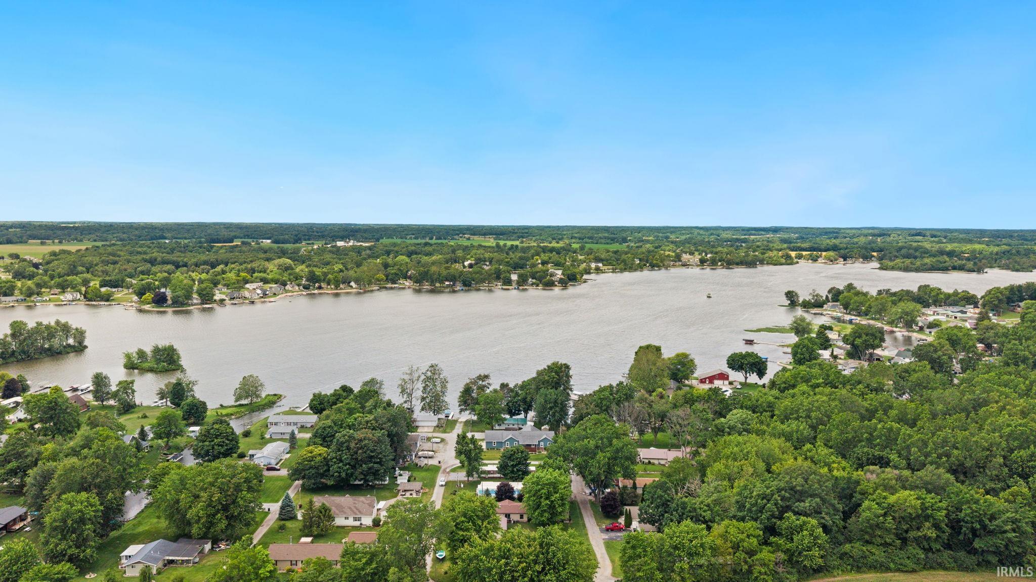 Image 2: Expansive lakefront setting featuring a clear blue sky, mature green trees, and residential properties bordering the water, Aerial View Image 2: Expansive lakefront setting featuring a clear blue sky, mature green trees, and residential properties bordering the water, Aerial View