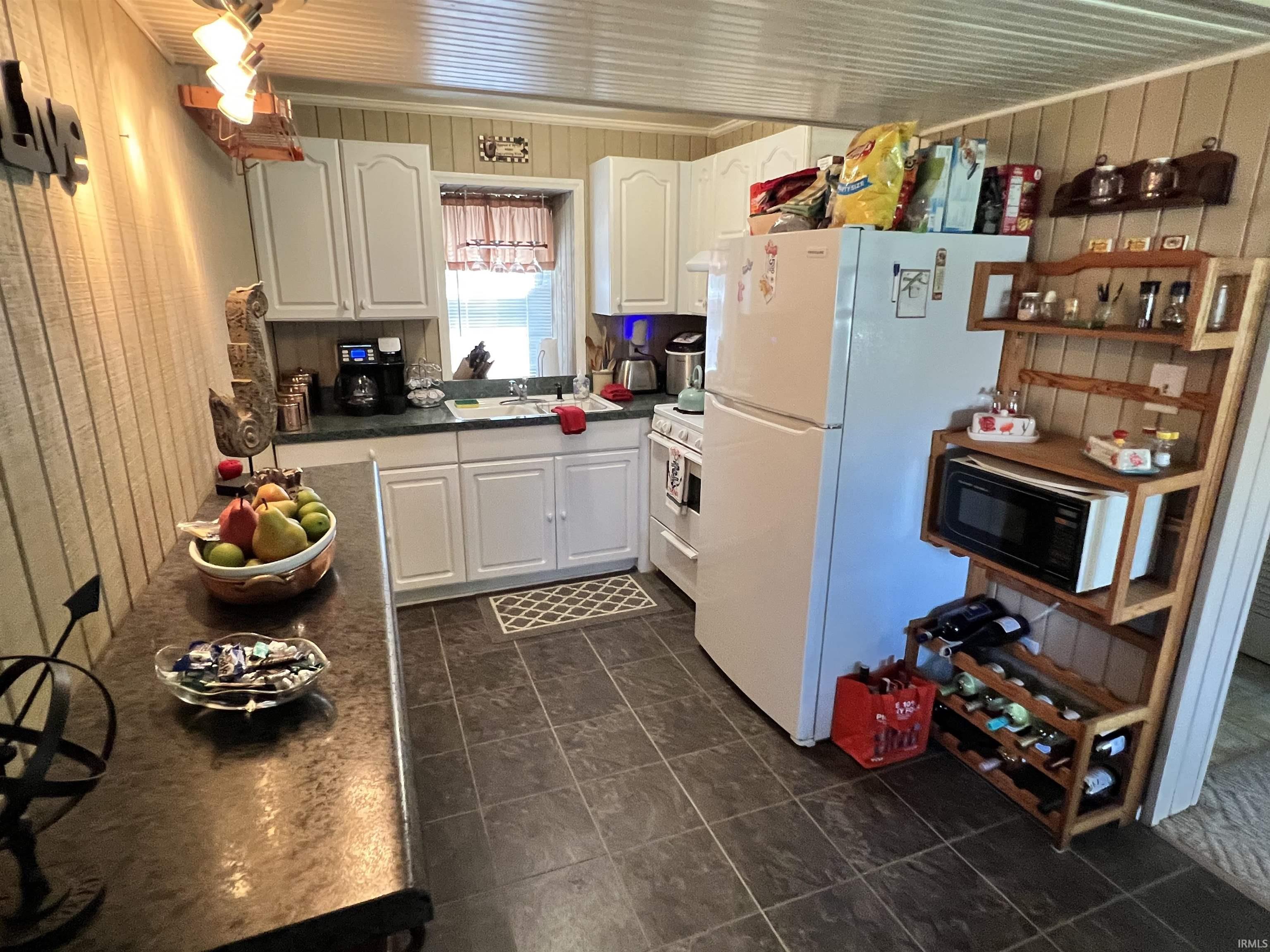 Image 1: Efficient kitchen featuring white cabinetry, dark countertop surfaces, a window above the sink, and tile flooring, Kitchen Image 1: Efficient kitchen featuring white cabinetry, dark countertop surfaces, a window above the sink, and tile flooring, Kitchen