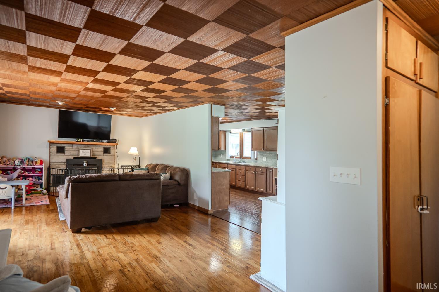 Image 3: Living area featuring checkerboard wood-finish ceiling, hardwood flooring, and a stone-clad fireplace, Living Room Image 3: Living area featuring checkerboard wood-finish ceiling, hardwood flooring, and a stone-clad fireplace, Living Room