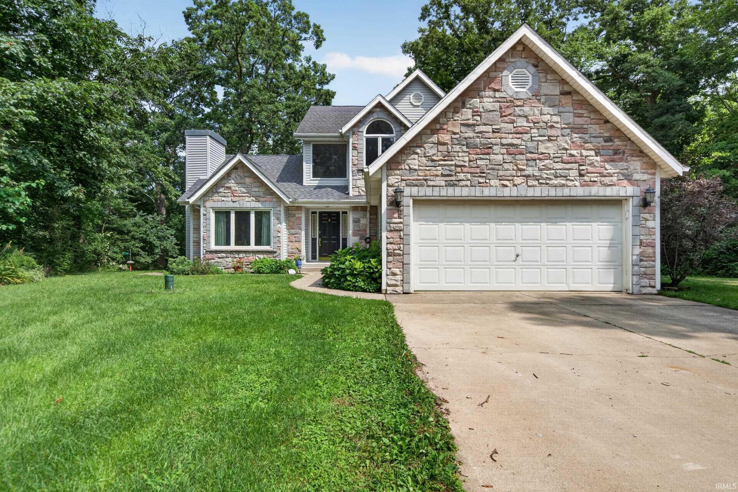 Image 1: Stone veneer facade, attached two-car garage, concrete driveway, arched window, and mature perimeter trees, Front Of Structure Image 1: Stone veneer facade, attached two-car garage, concrete driveway, arched window, and mature perimeter trees, Front Of Structure