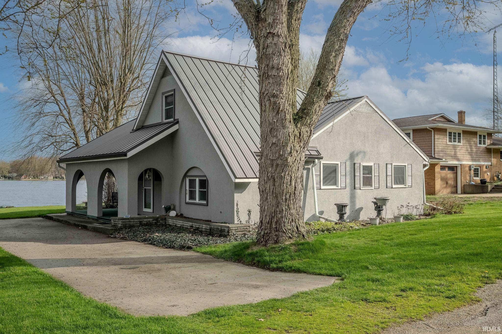 Image 1: View of home's exterior featuring covered porch, a standing seam roof, stucco siding, and a lawn, Side Of Structure Image 1: View of home's exterior featuring covered porch, a standing seam roof, stucco siding, and a lawn, Side Of Structure