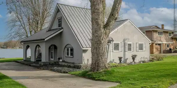 Image 1: View of home's exterior featuring covered porch, a standing seam roof, stucco siding, and a lawn, Side Of Structure Image 1: View of home's exterior featuring covered porch, a standing seam roof, stucco siding, and a lawn, Side Of Structure