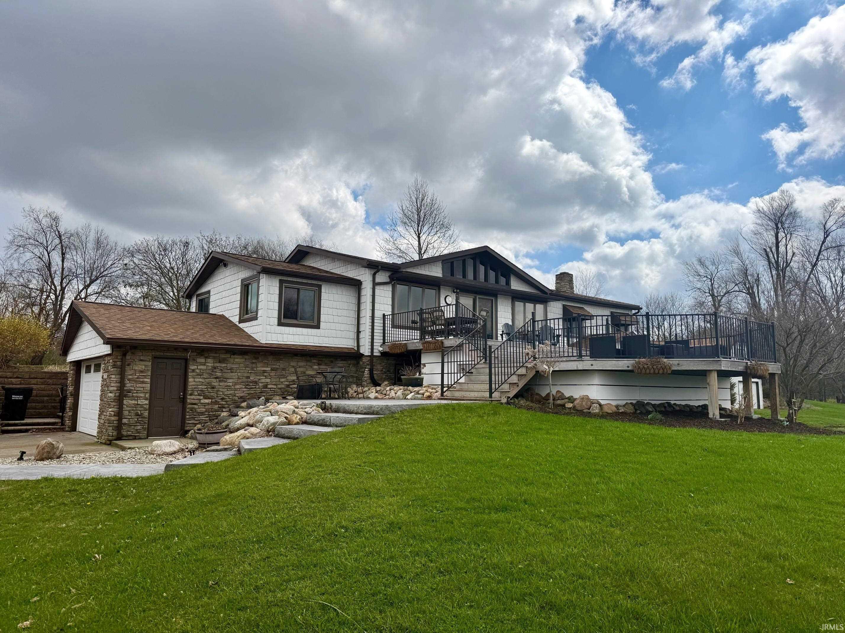 Image 0: View of front facade featuring stone siding, a wooden deck, a front lawn, and an attached garage, Front Of Structure