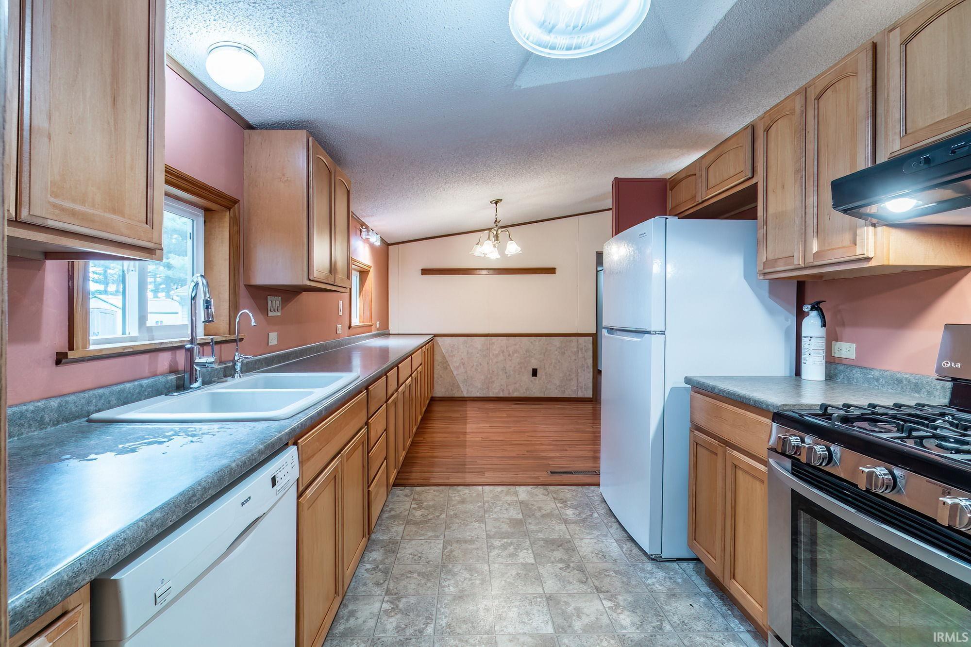 Image 3: Kitchen with white appliances, a wainscoted wall, dark countertops, hanging lights, and wood finish cabinets, Kitchen