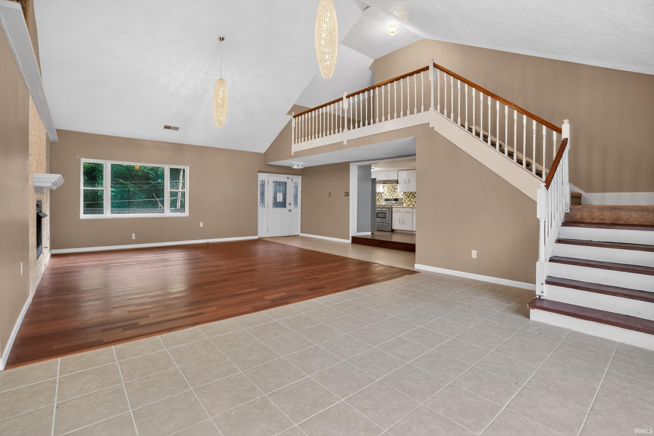 Image 2: Spacious interior featuring a vaulted ceiling and a prominent staircase with white balusters and wood-finish handrails, Living Room