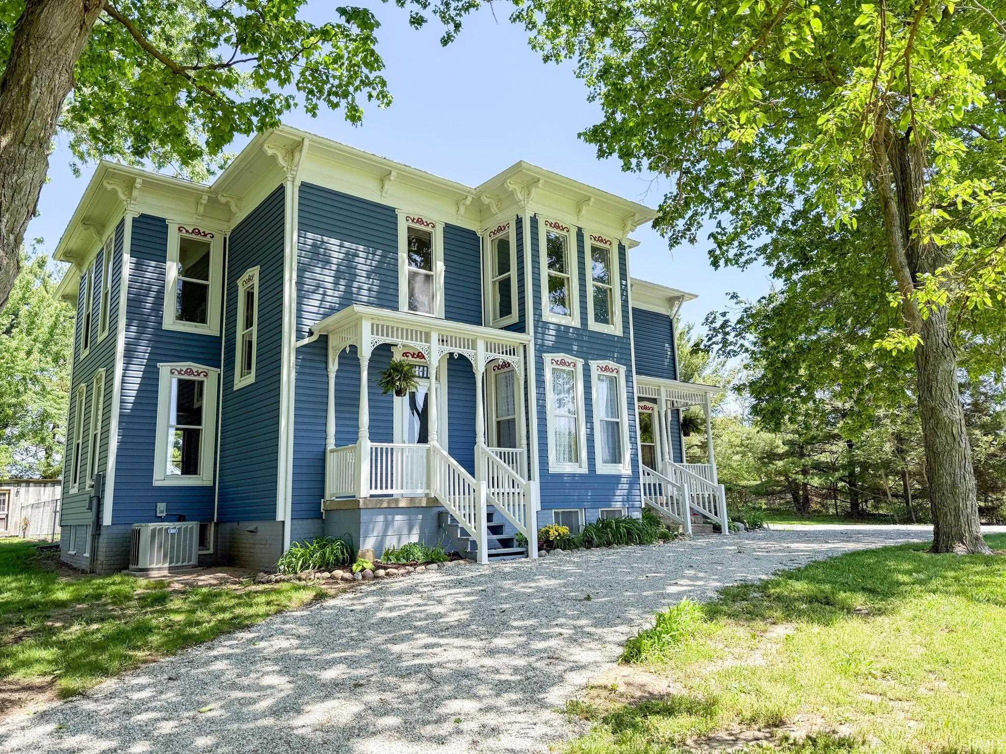Image 0: Two-story blue residence featuring white trim, a decorative front porch with white railings, and a gravel driveway, Front Of Structure Image 0: Two-story blue residence featuring white trim, a decorative front porch with white railings, and a gravel driveway, Front Of Structure