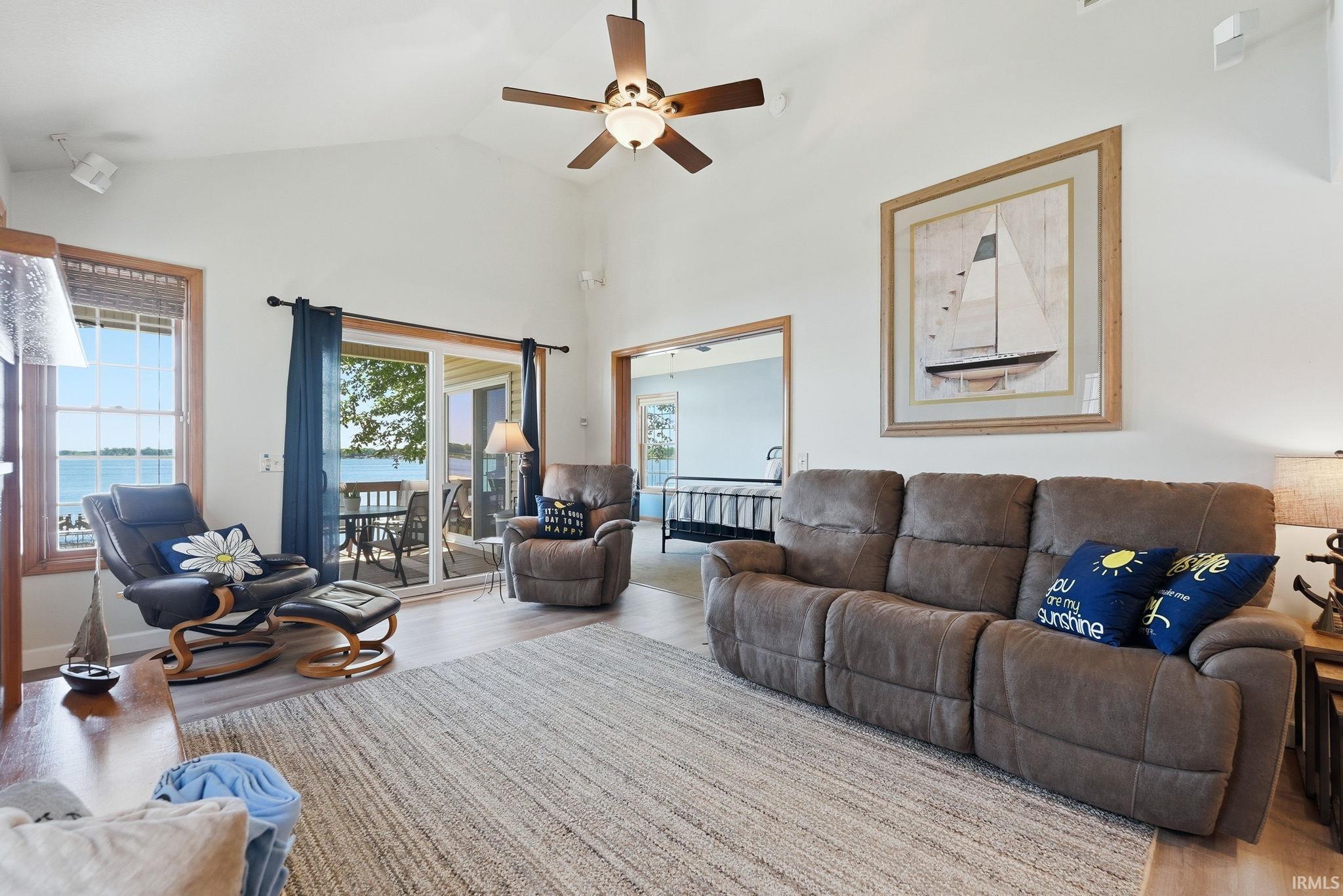 Image 2: Living area featuring vaulted ceilings, wood-finish flooring, a ceiling fan with integrated lighting, and a sliding glass door opening to an exterior deck, Living Room Image 2: Living area featuring vaulted ceilings, wood-finish flooring, a ceiling fan with integrated lighting, and a sliding glass door opening to an exterior deck, Living Room