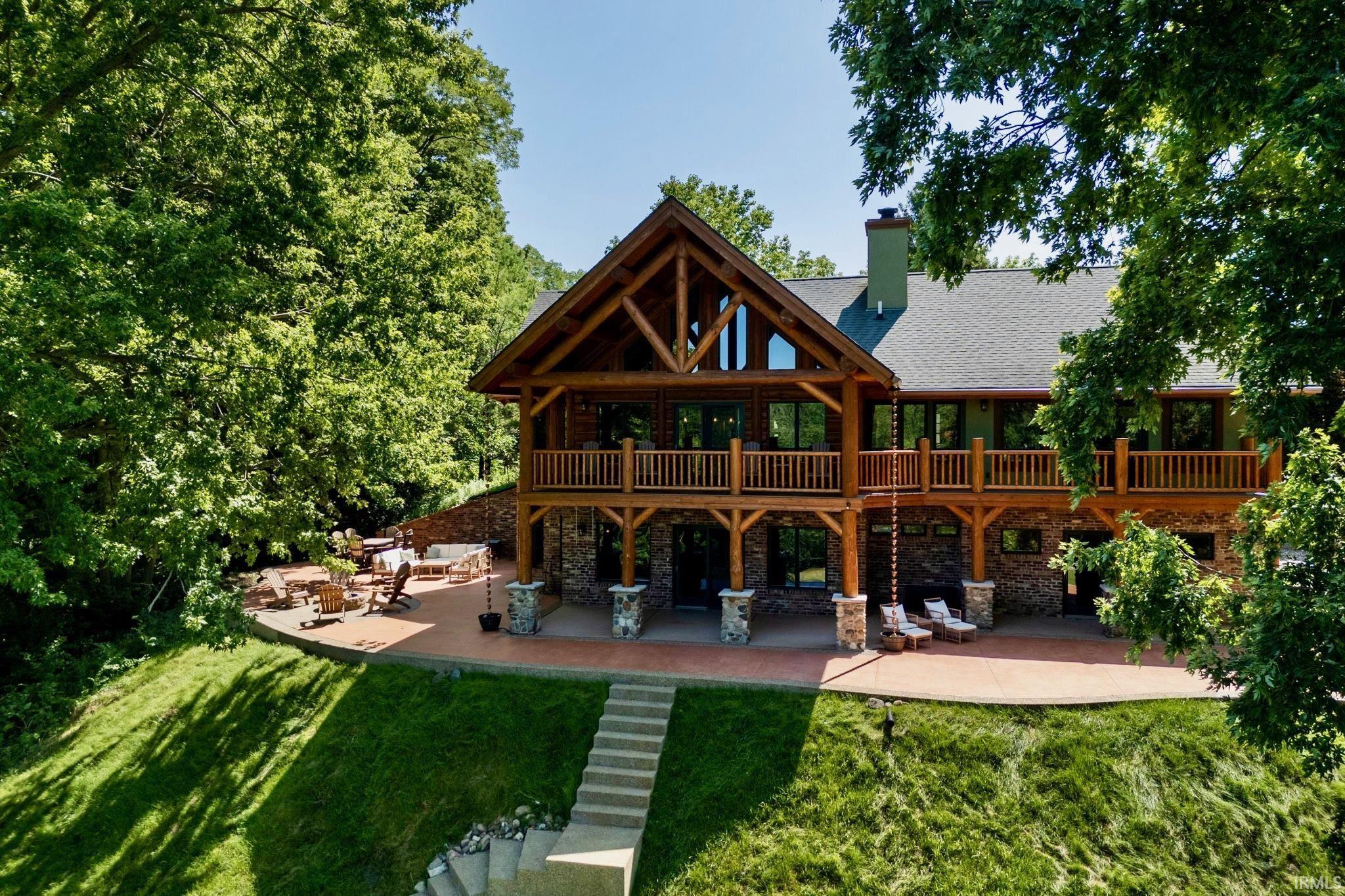 Image 0: Expansive timber-frame residence featuring multiple outdoor living areas, a lower-level patio, an upper-level balcony, stone pillars, and a prominent chimney, Back Of Structure