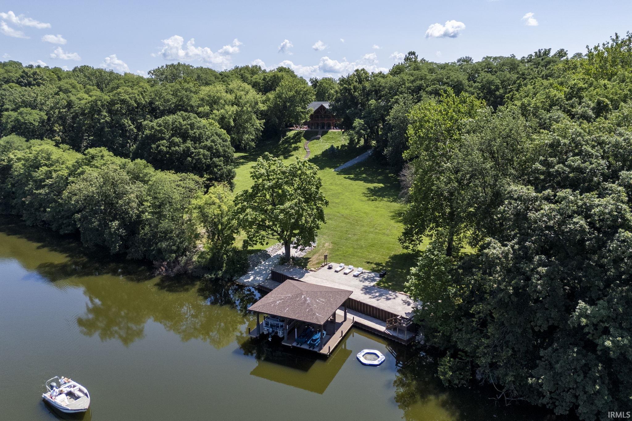 Image 1: Waterfront property featuring a private boat dock with covered slip, expansive waterside decking, and a sloped lawn surrounded by mature trees, Aerial View