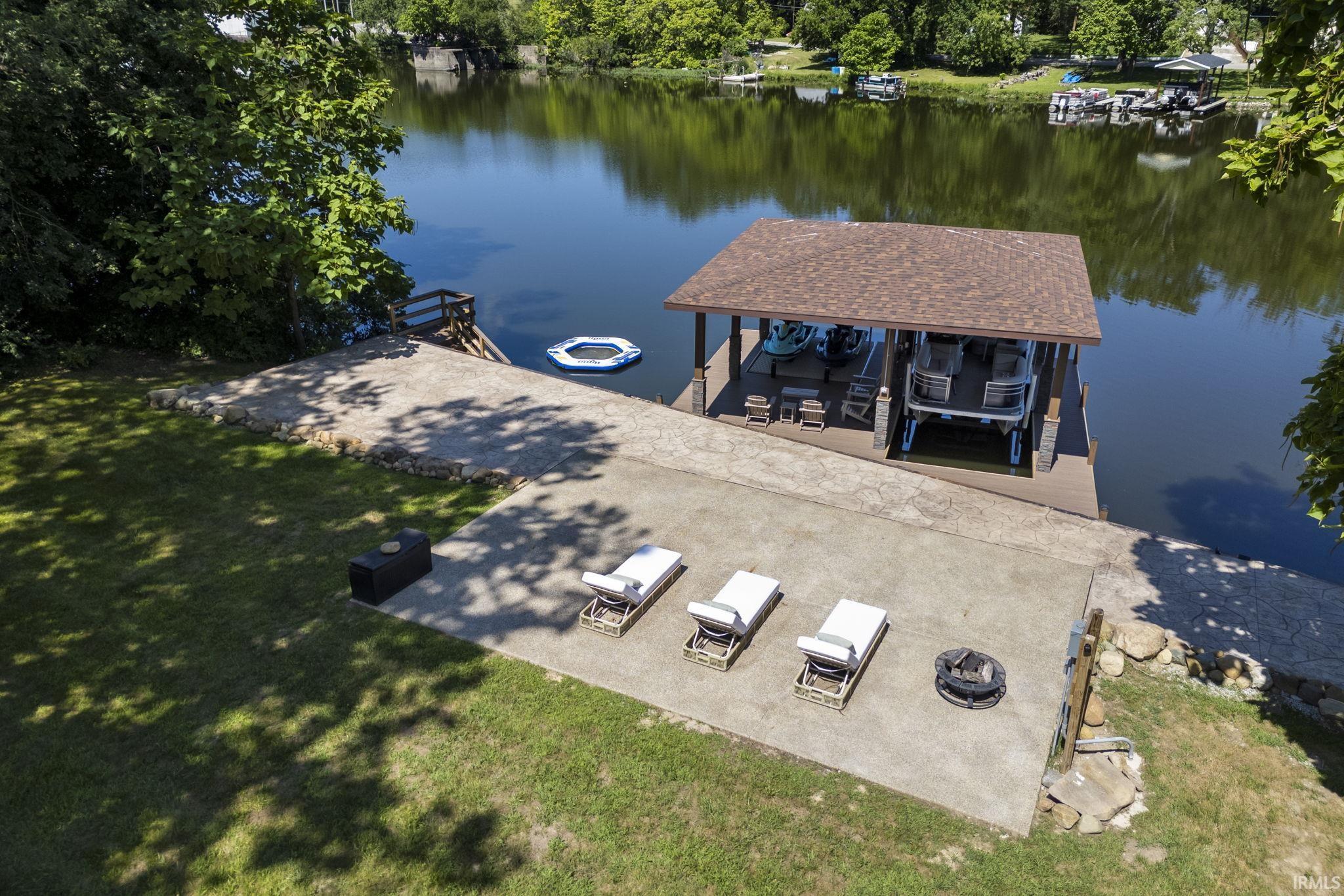 Image 2: Waterfront property featuring a private boat dock with a covered slip, a concrete patio, a built-in fire pit, and a landscaped shoreline with mature trees, Dock