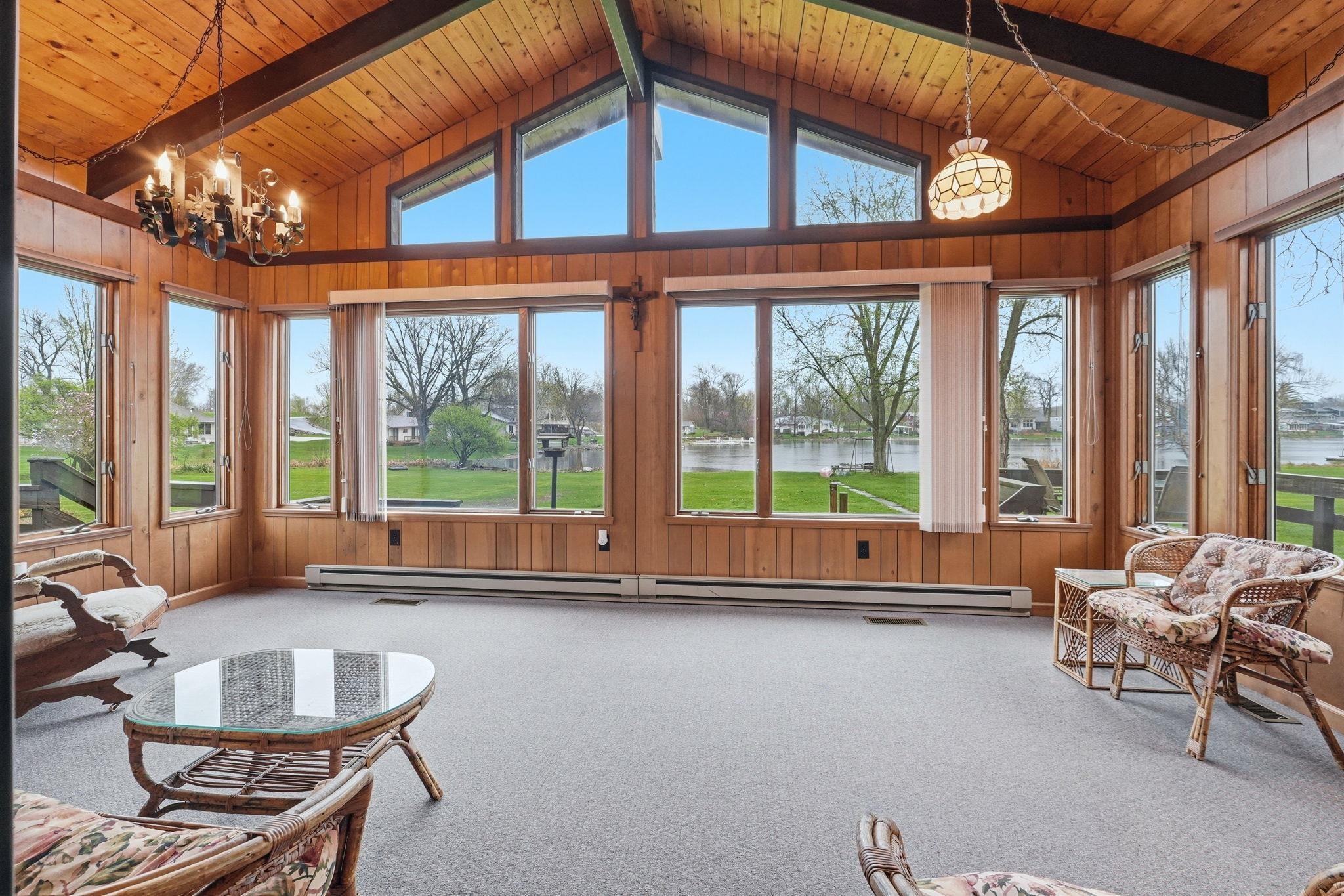 Image 1: Sunroom with suspended lighting, wood walls, carpet, a wooden ceiling with exposed beams, and healthy amount of natural light, Family Room Image 1: Sunroom with suspended lighting, wood walls, carpet, a wooden ceiling with exposed beams, and healthy amount of natural light, Family Room