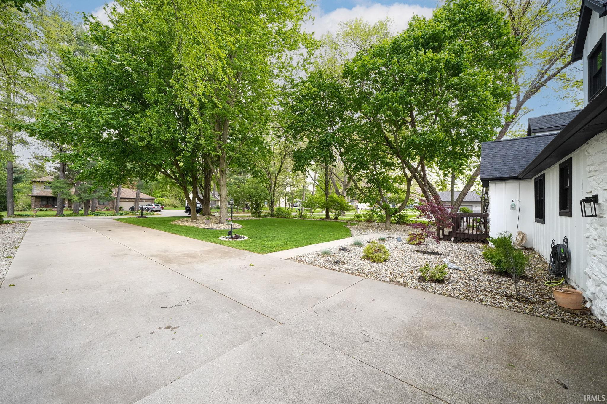 Image 2: Expansive concrete driveway with a manicured lawn area and mature trees, Patio