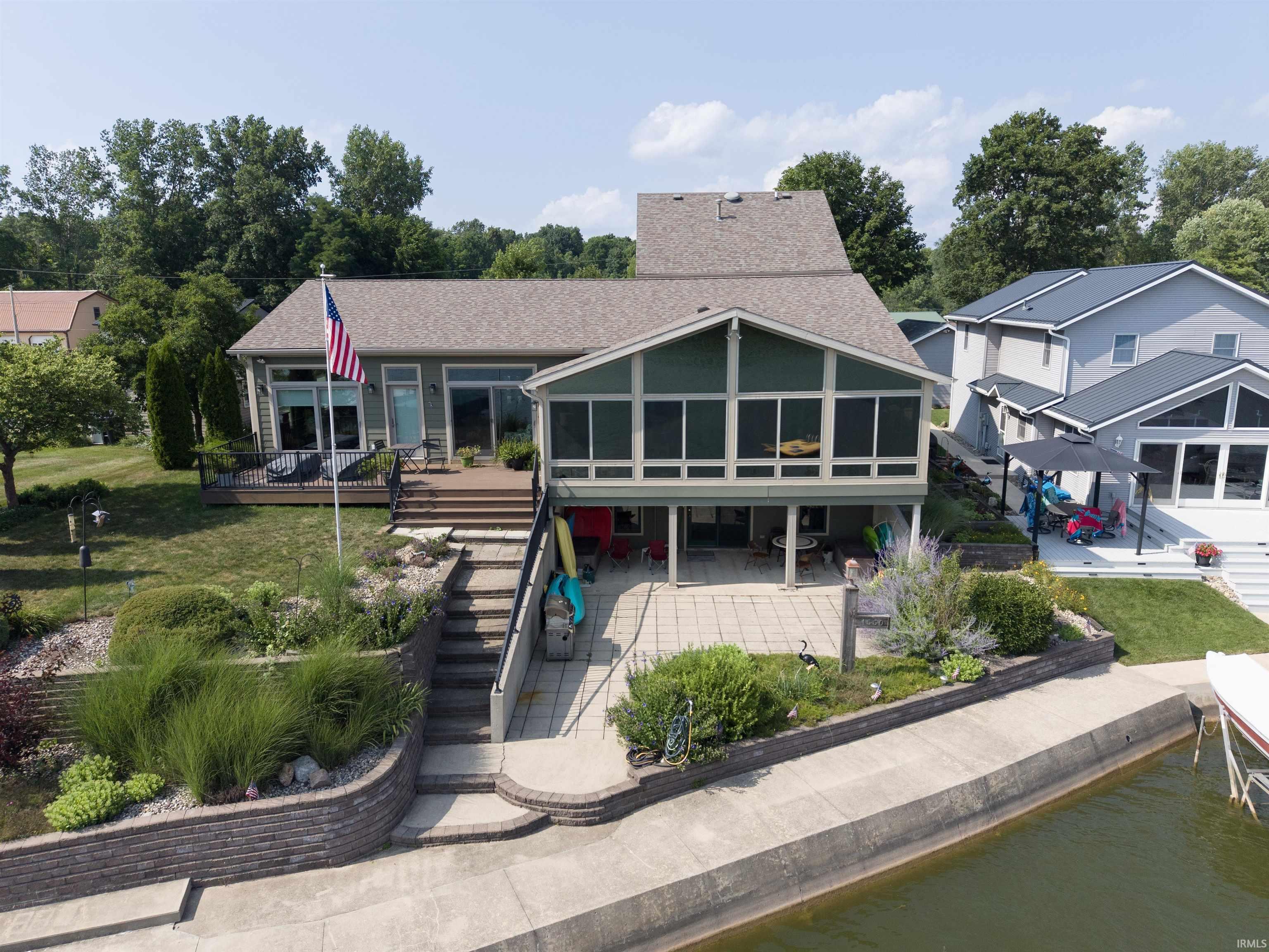 Image 2: Waterside property featuring a multi-level concrete retaining wall, a paved patio, and a screened porch, Back Of Structure Image 2: Waterside property featuring a multi-level concrete retaining wall, a paved patio, and a screened porch, Back Of Structure