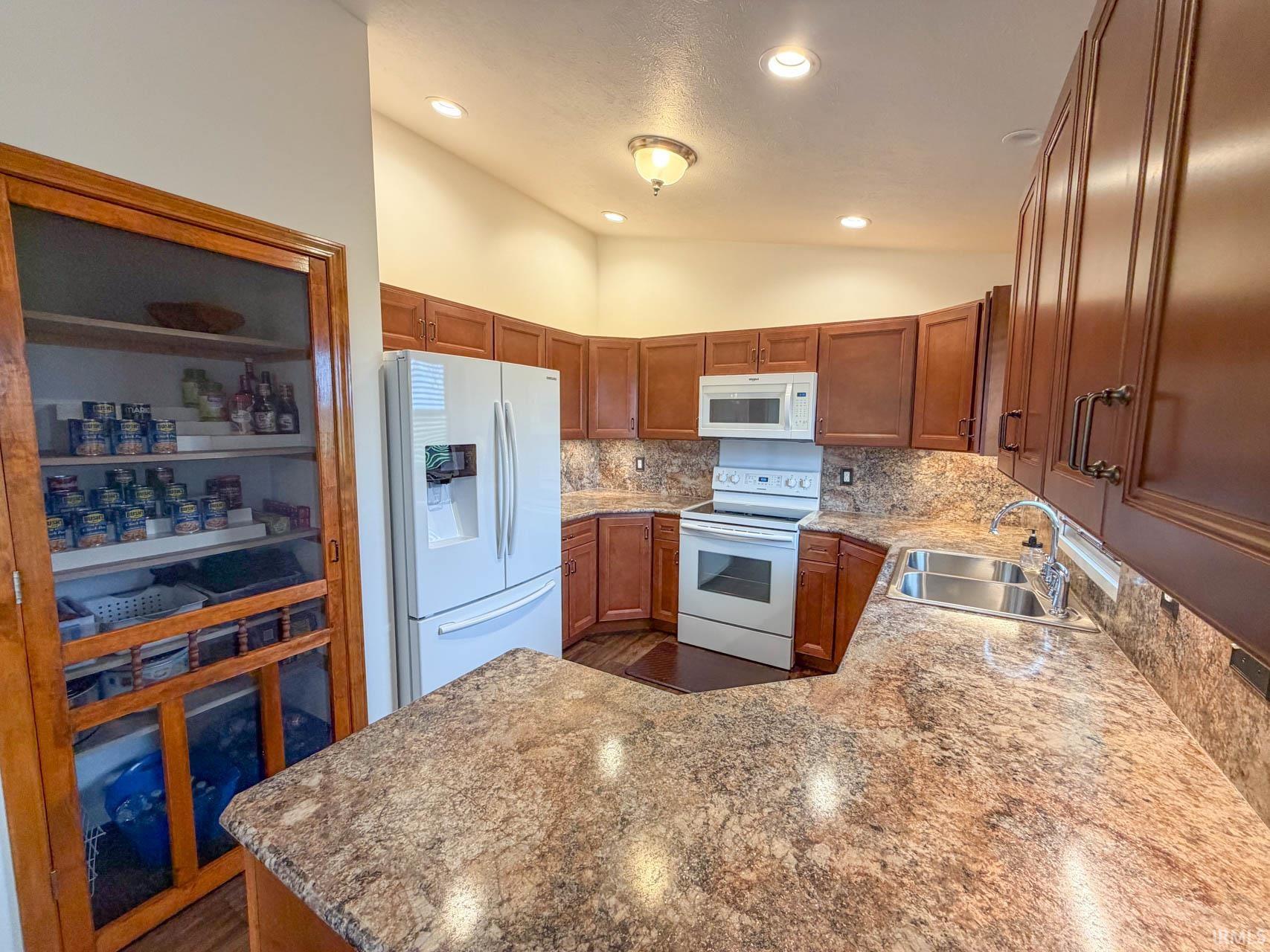 Image 3: Kitchen with white appliances, light stone countertops, decorative backsplash, wood finish cabinetry, and a peninsula, Kitchen