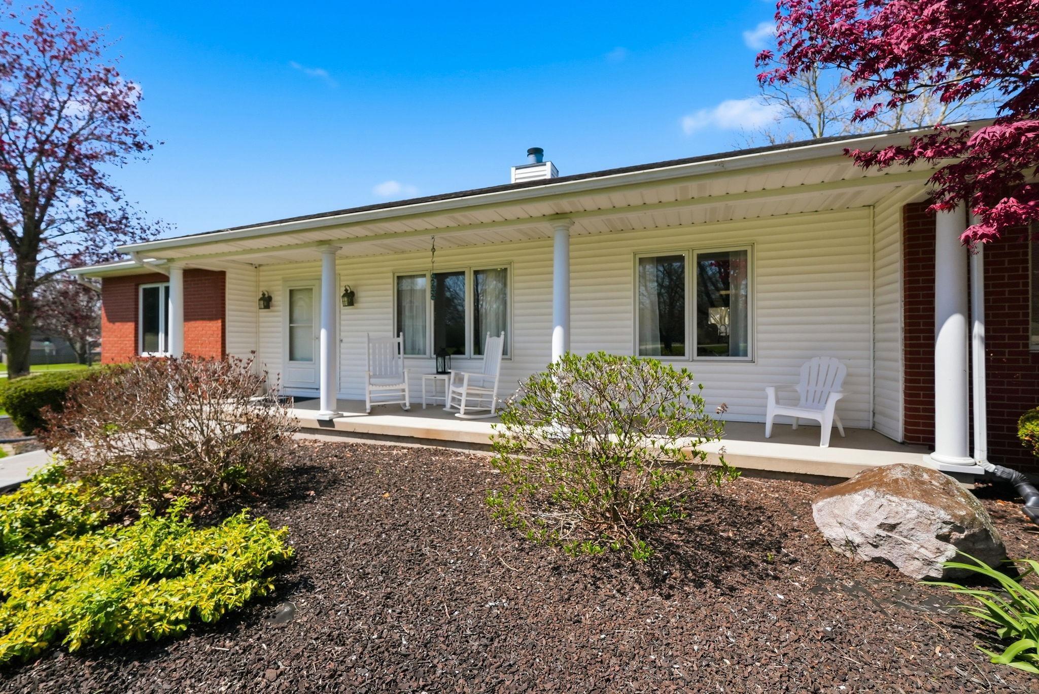 Image 2: Exterior featuring white siding, brick accents, a covered front porch, and established landscaping with shrubbery and trees, Front Of Structure Image 2: Exterior featuring white siding, brick accents, a covered front porch, and established landscaping with shrubbery and trees, Front Of Structure