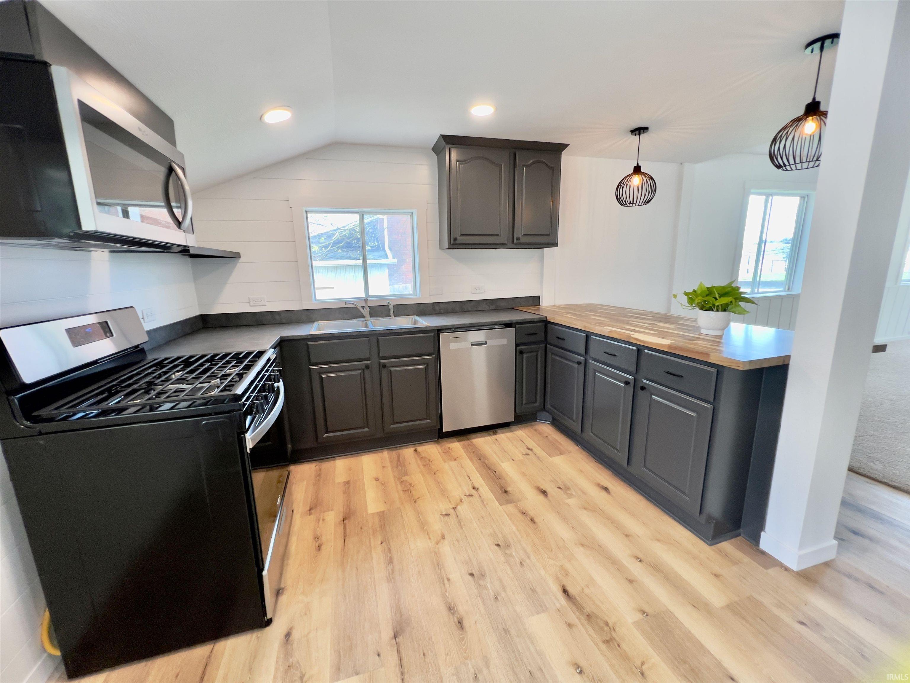 Image 1: Modern kitchen featuring dark cabinetry, vinyl plank flooring, stainless steel appliances, a butcher block countertop extension, and shiplap wall accents, Kitchen Image 1: Modern kitchen featuring dark cabinetry, vinyl plank flooring, stainless steel appliances, a butcher block countertop extension, and shiplap wall accents, Kitchen