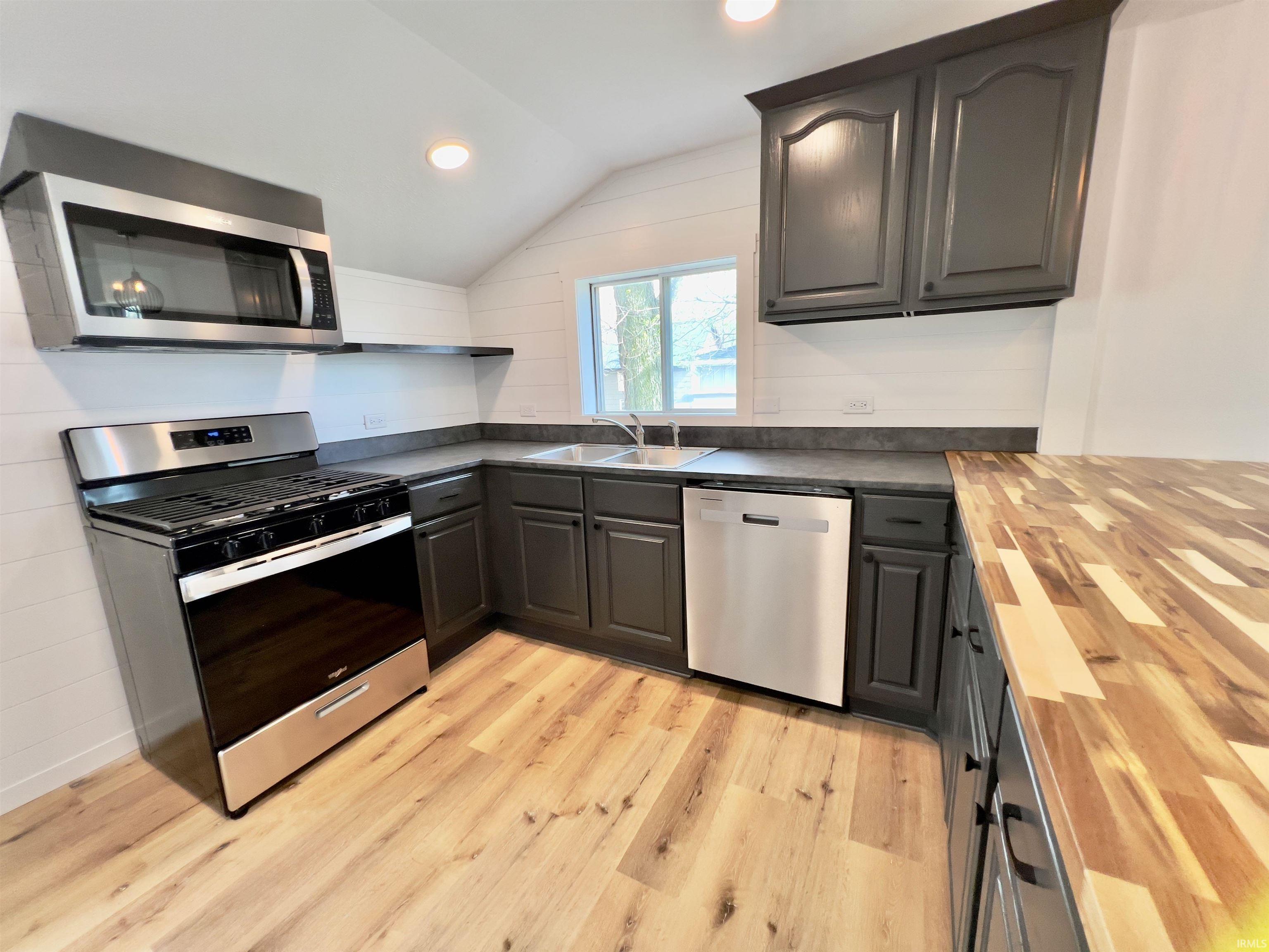 Image 2: Kitchen featuring stainless steel appliances, dark cabinetry, light wood-finish flooring, butcher block countertop, and shiplap wall paneling, Kitchen Image 2: Kitchen featuring stainless steel appliances, dark cabinetry, light wood-finish flooring, butcher block countertop, and shiplap wall paneling, Kitchen