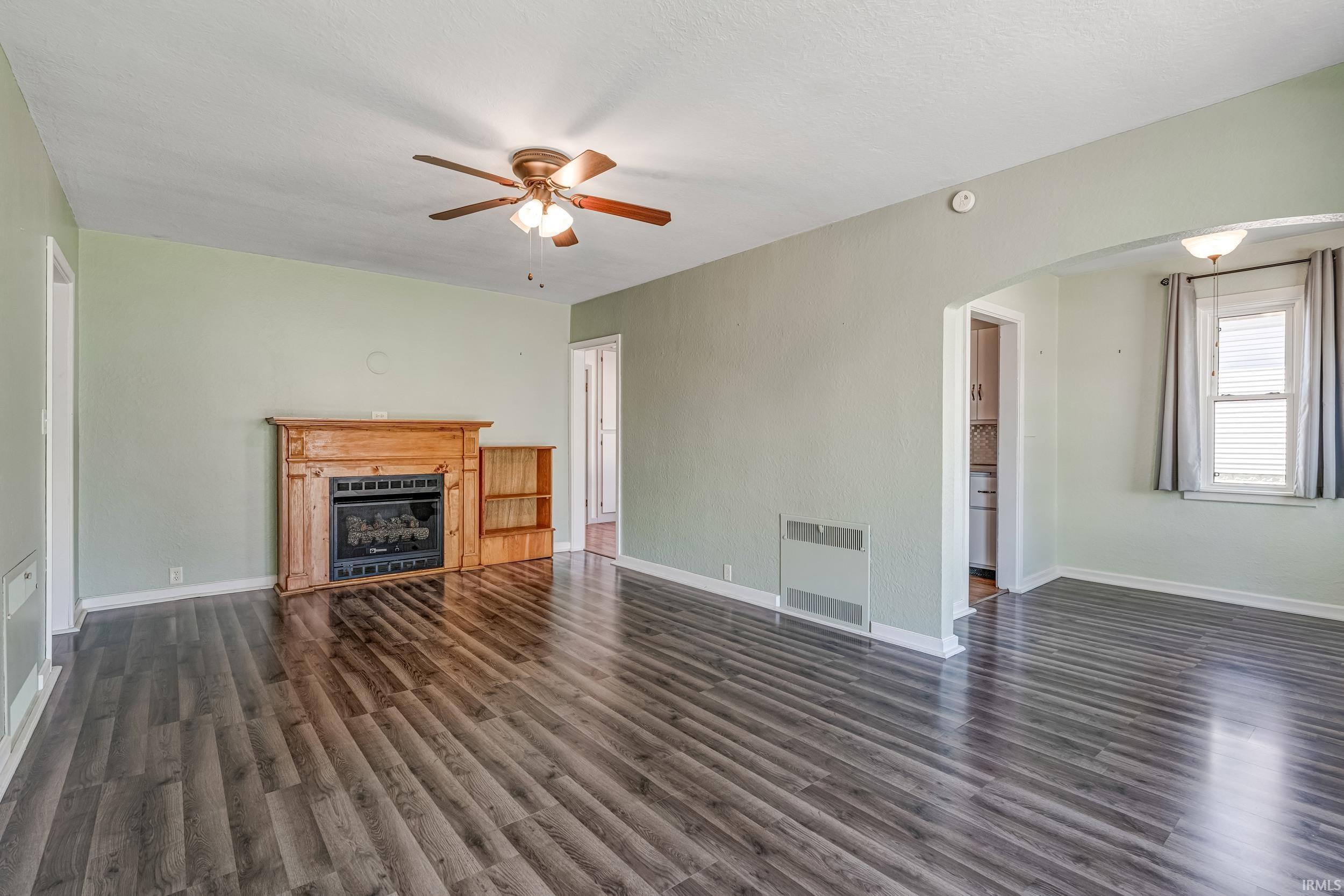 Image 2: Spacious living area featuring wood-finish flooring, a fireplace with a detailed wooden mantel, and a ceiling fan with integrated lighting, Living Room Image 2: Spacious living area featuring wood-finish flooring, a fireplace with a detailed wooden mantel, and a ceiling fan with integrated lighting, Living Room