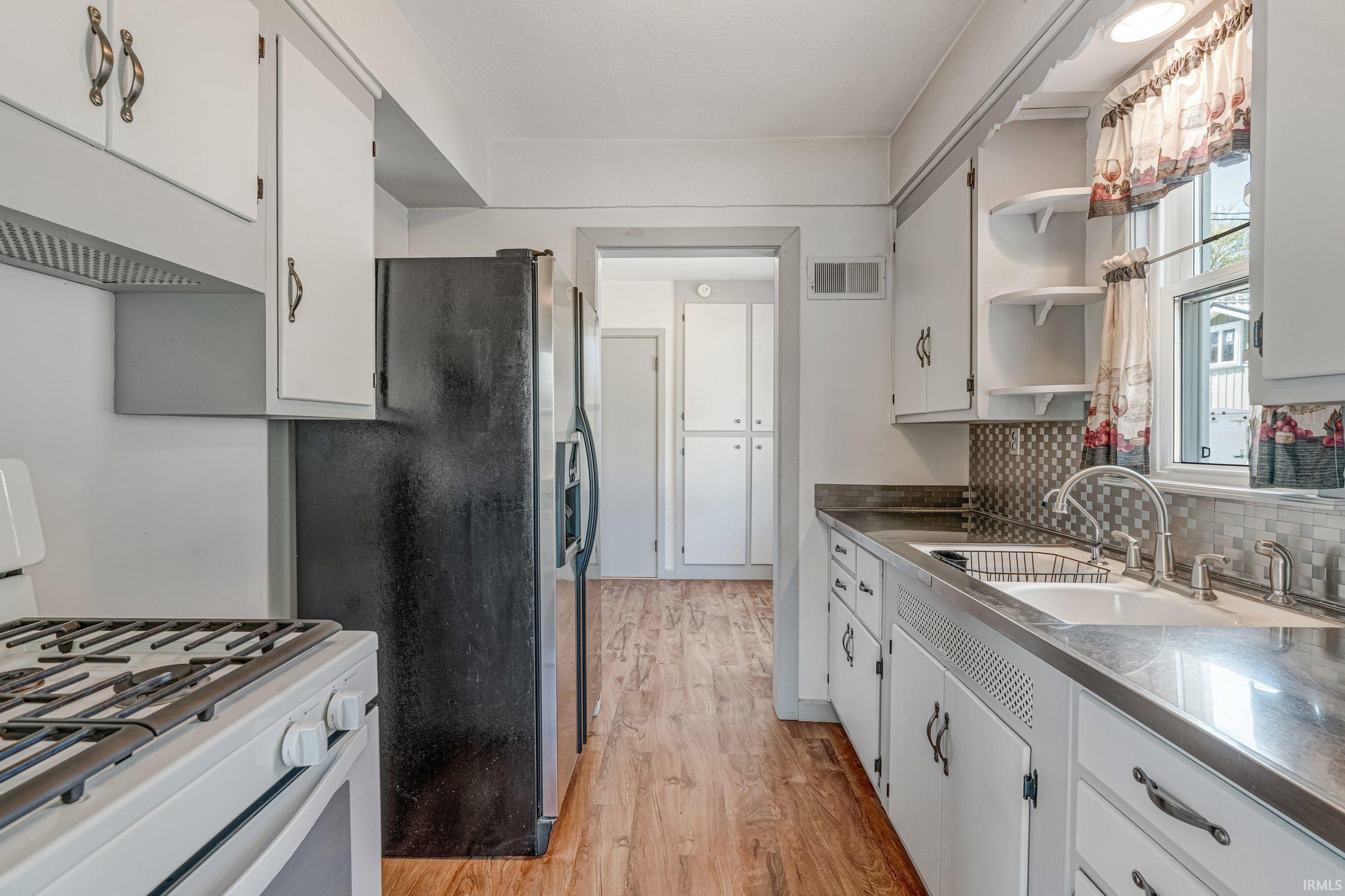 Image 3: Kitchen featuring white cabinetry with dark hardware, a black refrigerator, and wood-finish flooring, Kitchen Image 3: Kitchen featuring white cabinetry with dark hardware, a black refrigerator, and wood-finish flooring, Kitchen