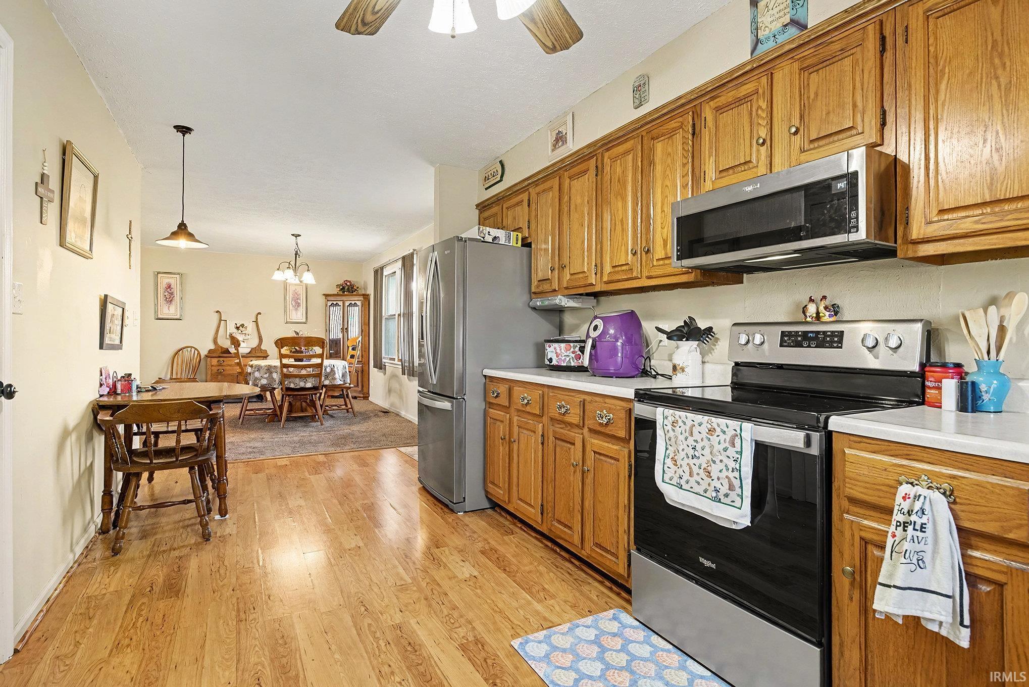 Image 3: Kitchen with appliances with stainless steel finishes, brown cabinets, light countertops, and hanging light fixtures, Kitchen