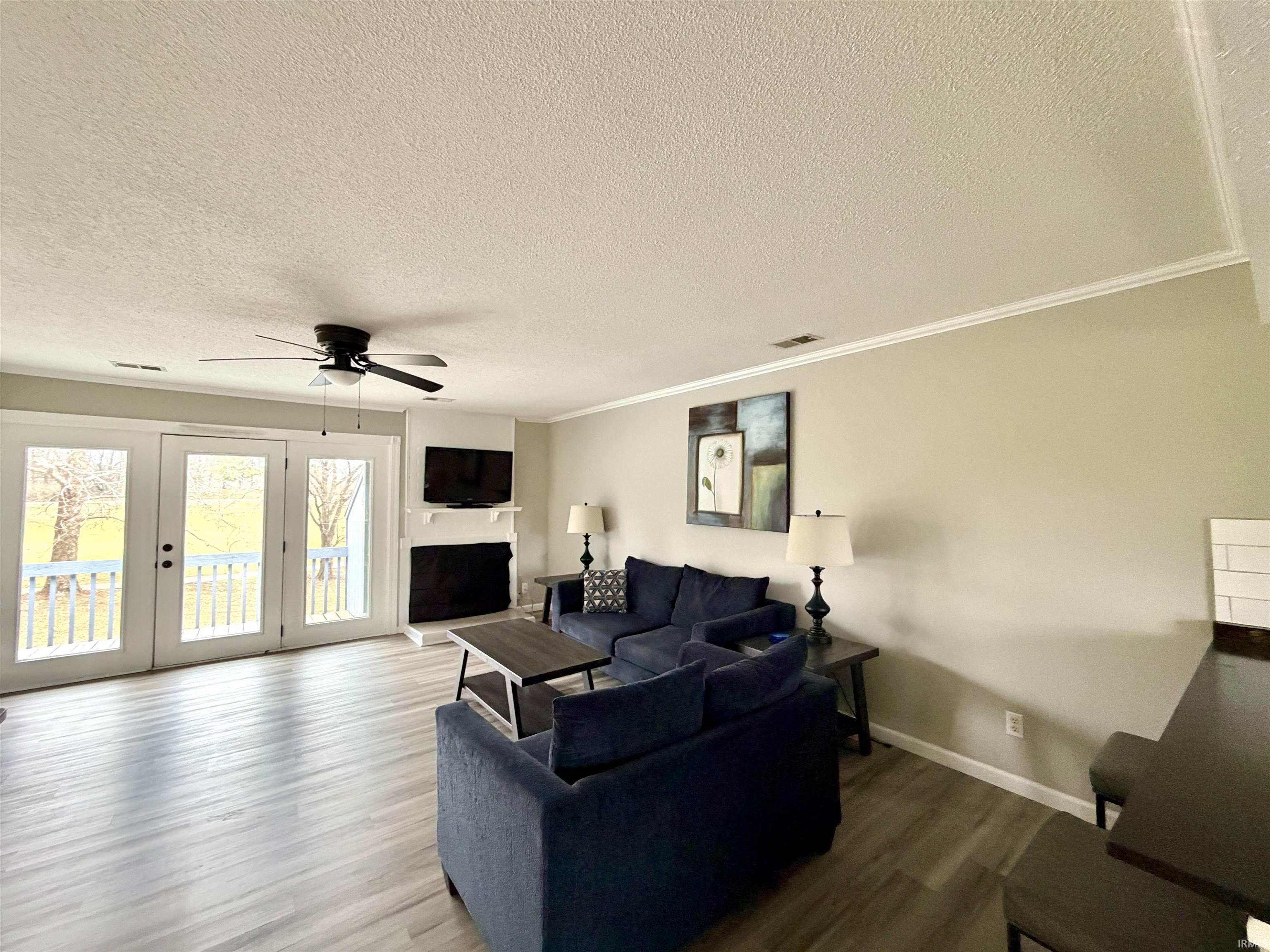 Image 2: Living area with wood finished floors, a textured ceiling, a fireplace with raised hearth, a ceiling fan, and ornamental molding, Living Room