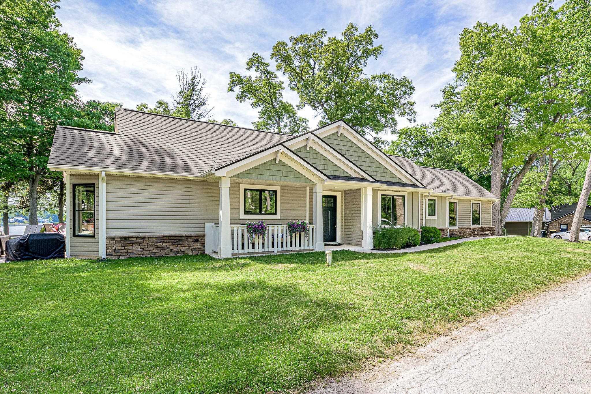 Image 2: Contemporary residence featuring a covered front porch with white railing, a dark entry door, light siding with stone accents, a multi-pitched roofline, and established landscaping, Front Of Structure
