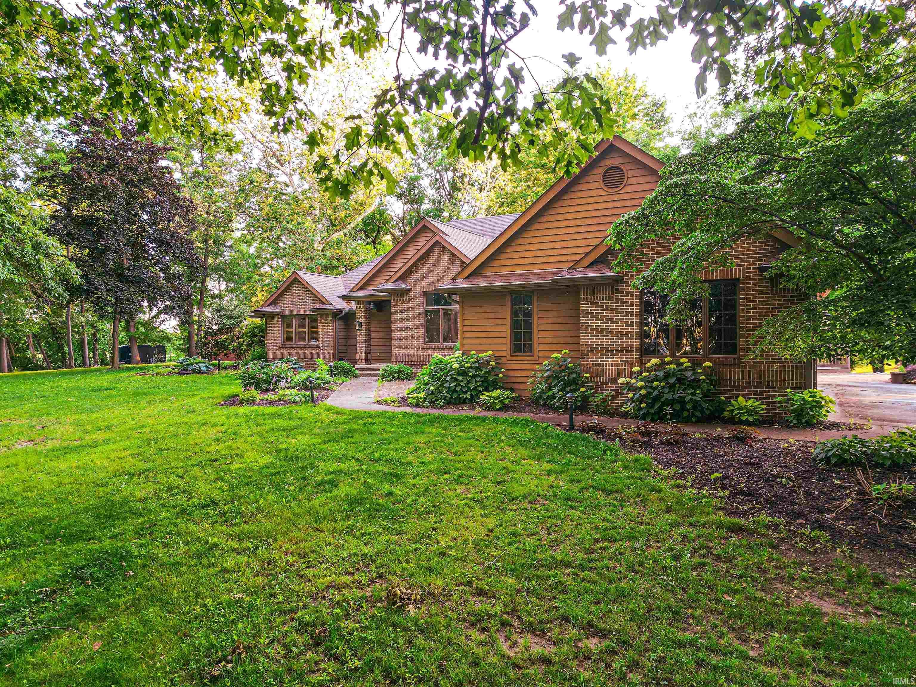 Image 2: Brick and wood-sided exterior featuring multiple gables, a manicured lawn, mature trees, and established shrubbery with blooming hydrangeas, Front Of Structure Image 2: Brick and wood-sided exterior featuring multiple gables, a manicured lawn, mature trees, and established shrubbery with blooming hydrangeas, Front Of Structure