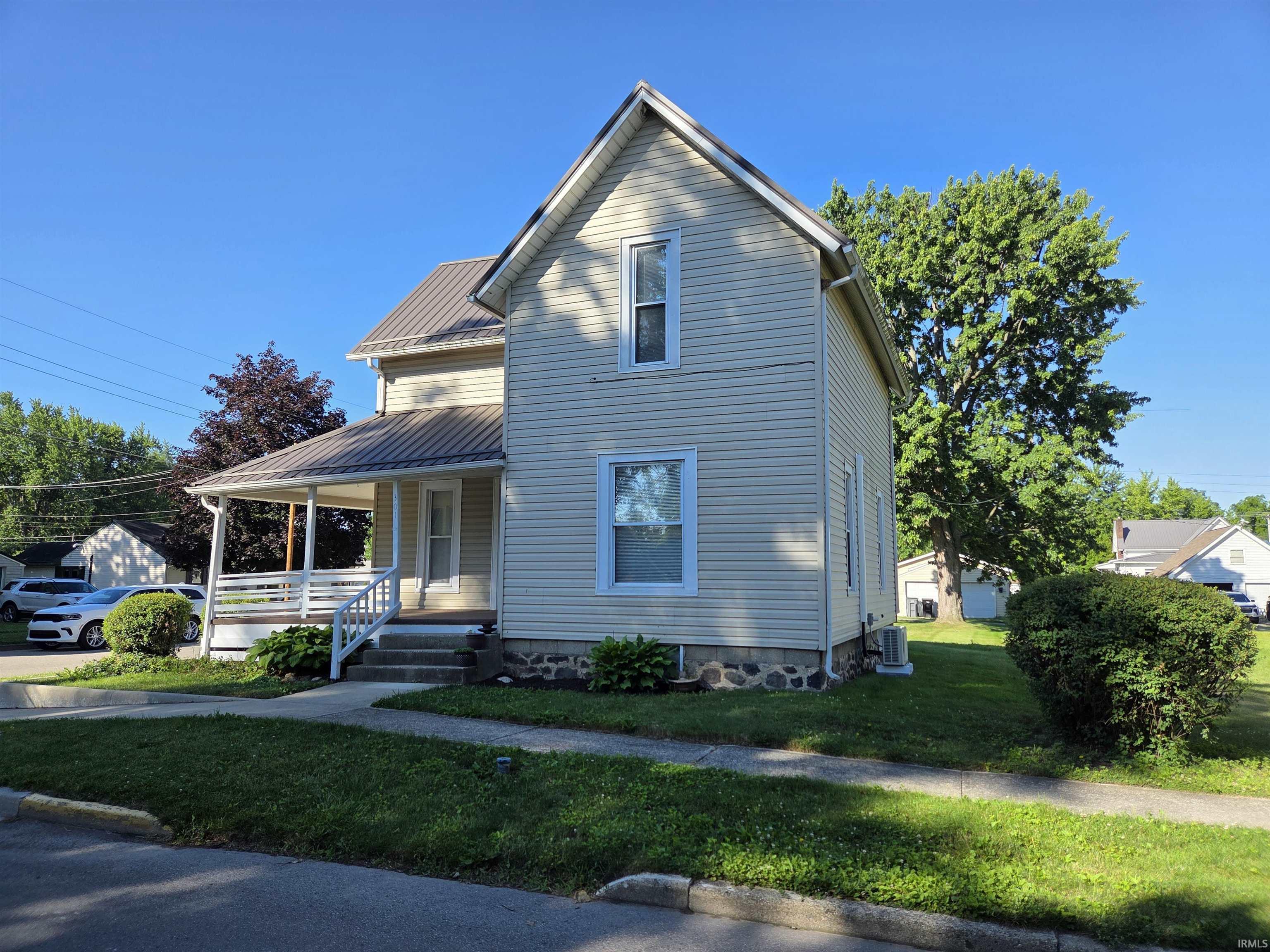 Image 1: Two-story residence featuring light-colored siding, a metal roof, and a covered front porch with white railings, Front Of Structure Image 1: Two-story residence featuring light-colored siding, a metal roof, and a covered front porch with white railings, Front Of Structure