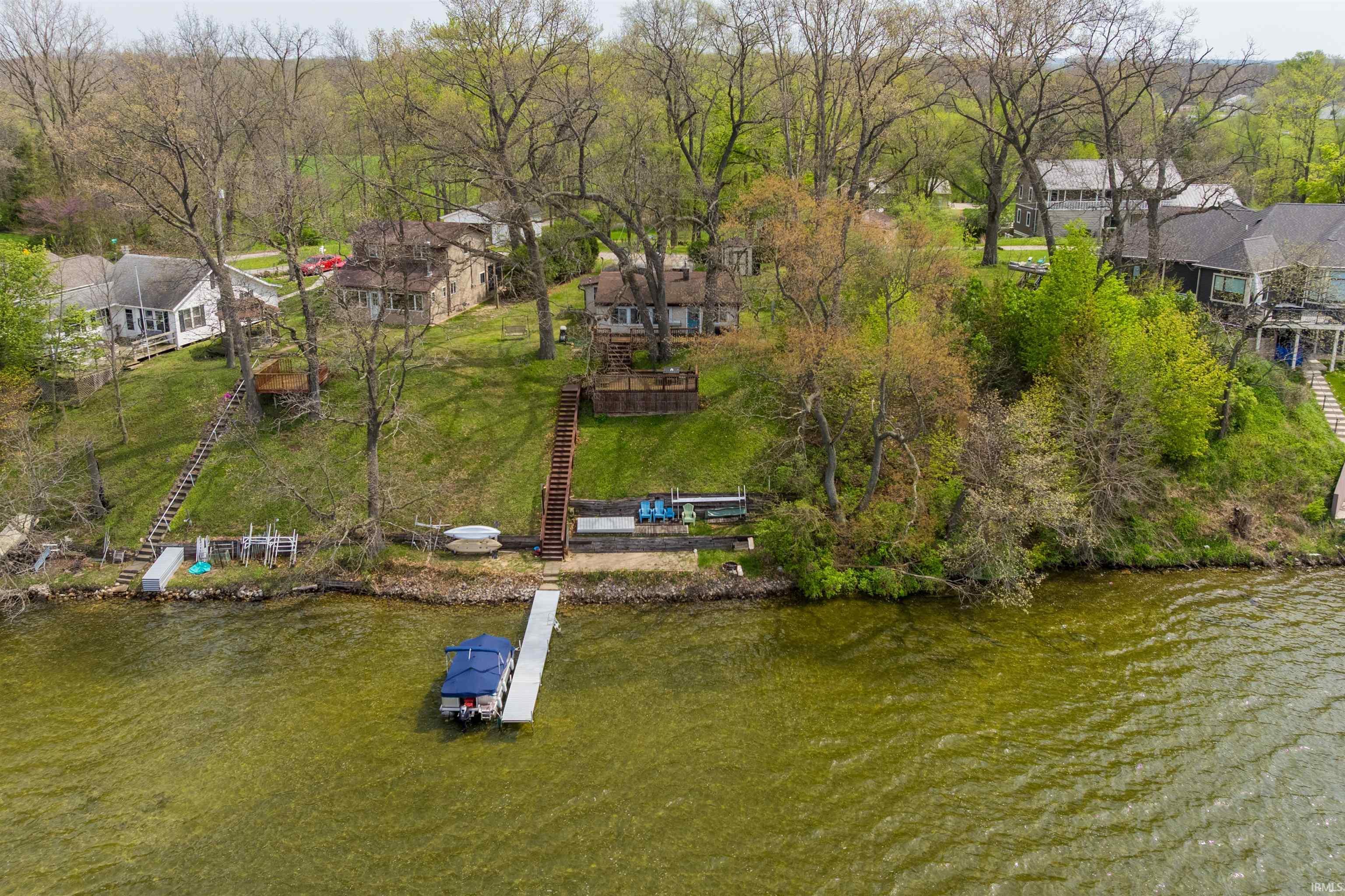 Image 0: Lakeside property featuring a boat dock, tiered wooden stairway access to the water, and a sloped, tree-lined lawn, Aerial View Image 0: Lakeside property featuring a boat dock, tiered wooden stairway access to the water, and a sloped, tree-lined lawn, Aerial View