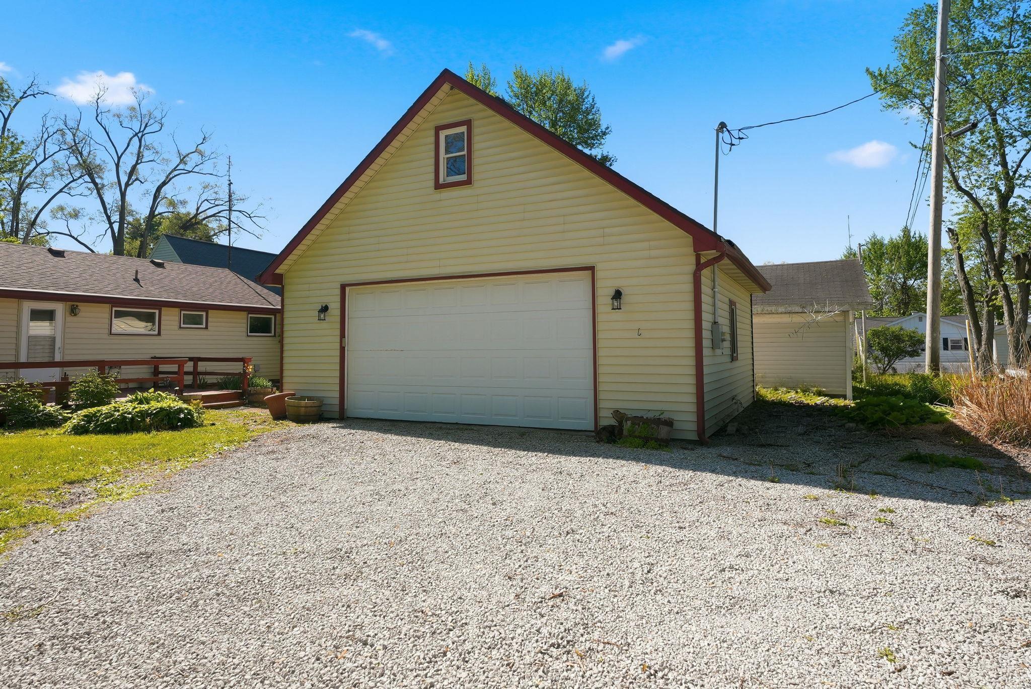 Image 1: Detached garage structure with light-colored siding, a white overhead door, and a red-trimmed gable roof, Garage Image 1: Detached garage structure with light-colored siding, a white overhead door, and a red-trimmed gable roof, Garage