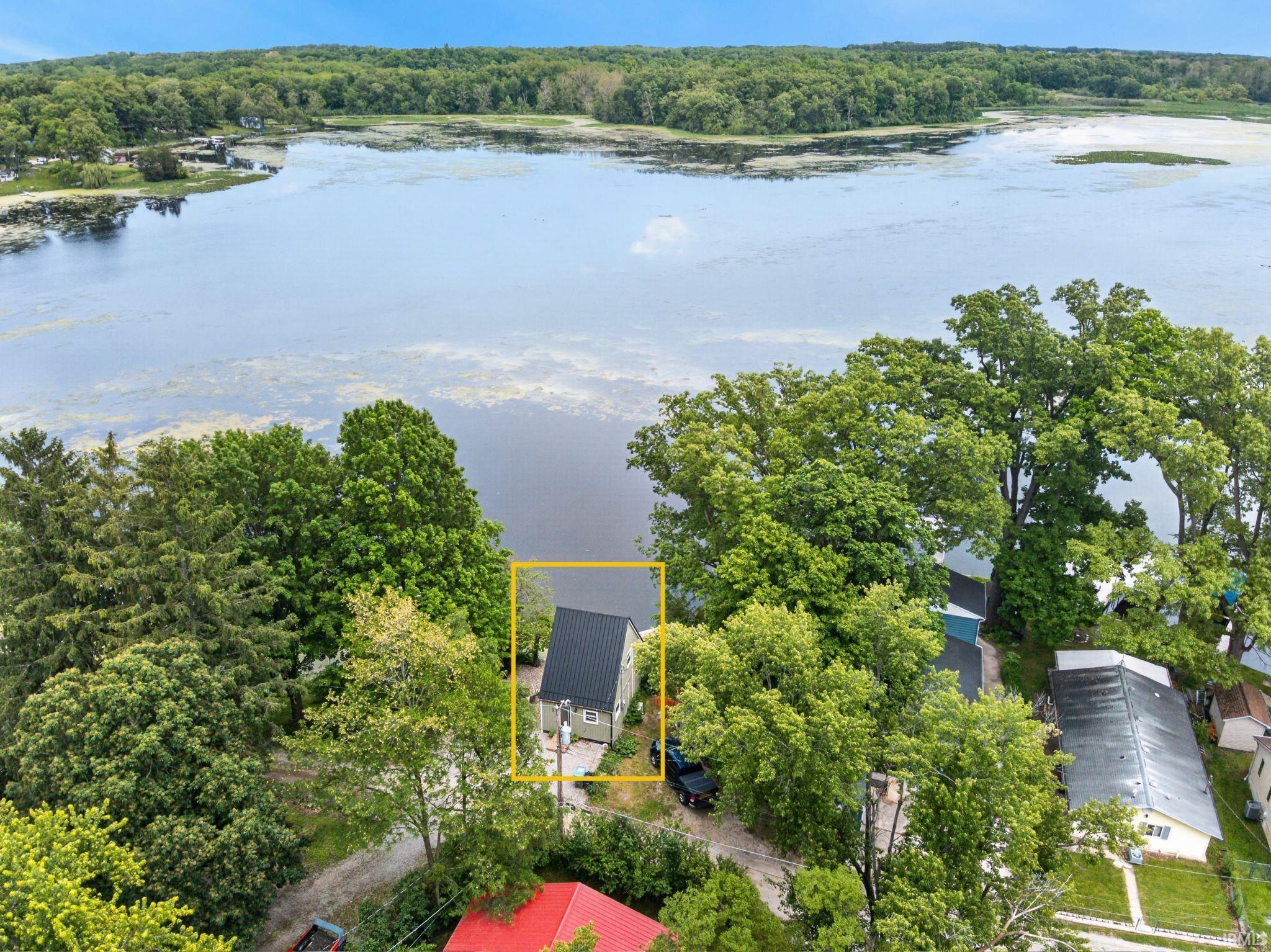 Image 1: Waterfront property featuring a pitched roofline, light-colored siding, and mature tree coverage, Aerial View Image 1: Waterfront property featuring a pitched roofline, light-colored siding, and mature tree coverage, Aerial View