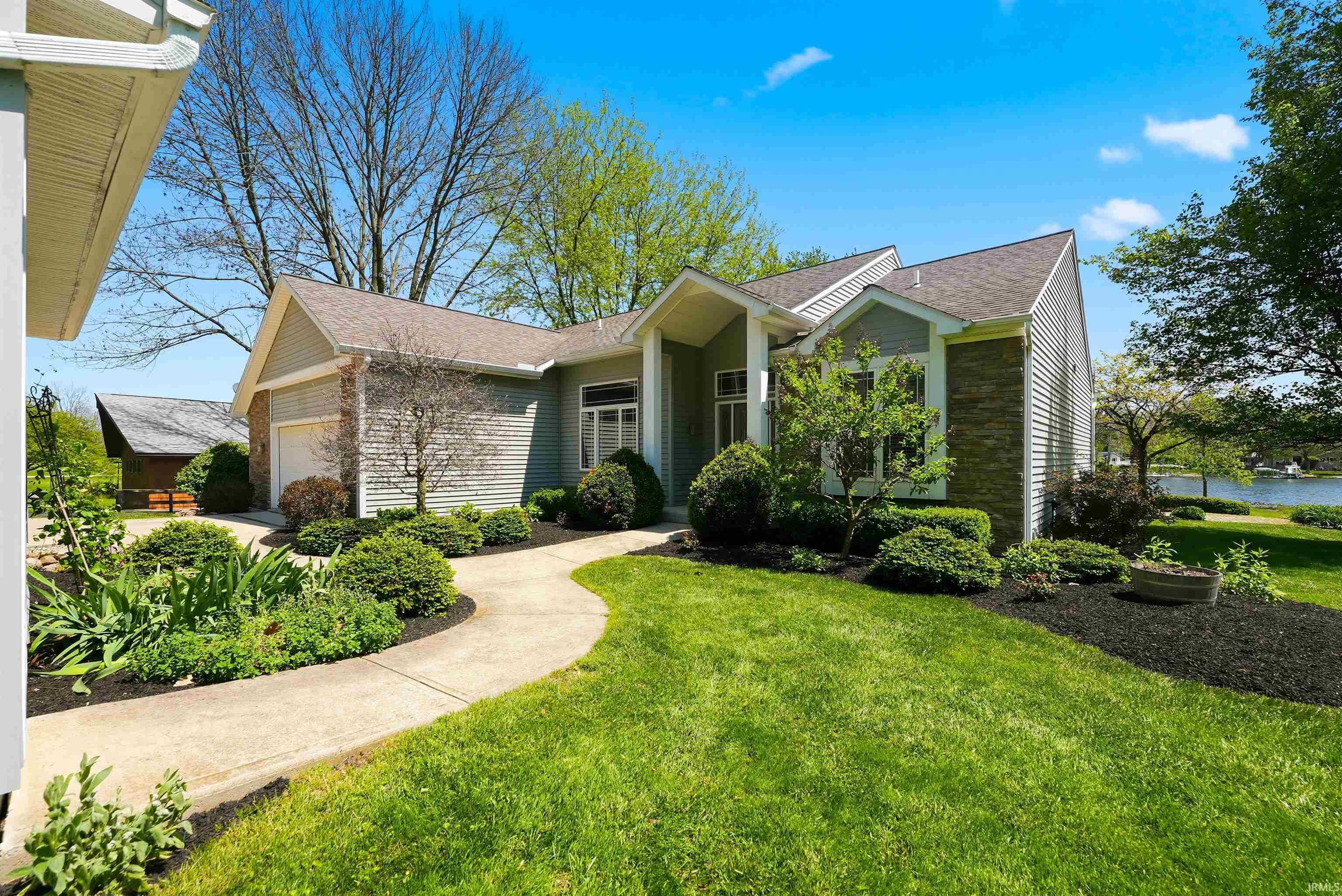 Image 1: Single-story residence featuring light gray siding with brick accents, an attached garage, and a winding concrete pathway, Front Of Structure Image 1: Single-story residence featuring light gray siding with brick accents, an attached garage, and a winding concrete pathway, Front Of Structure