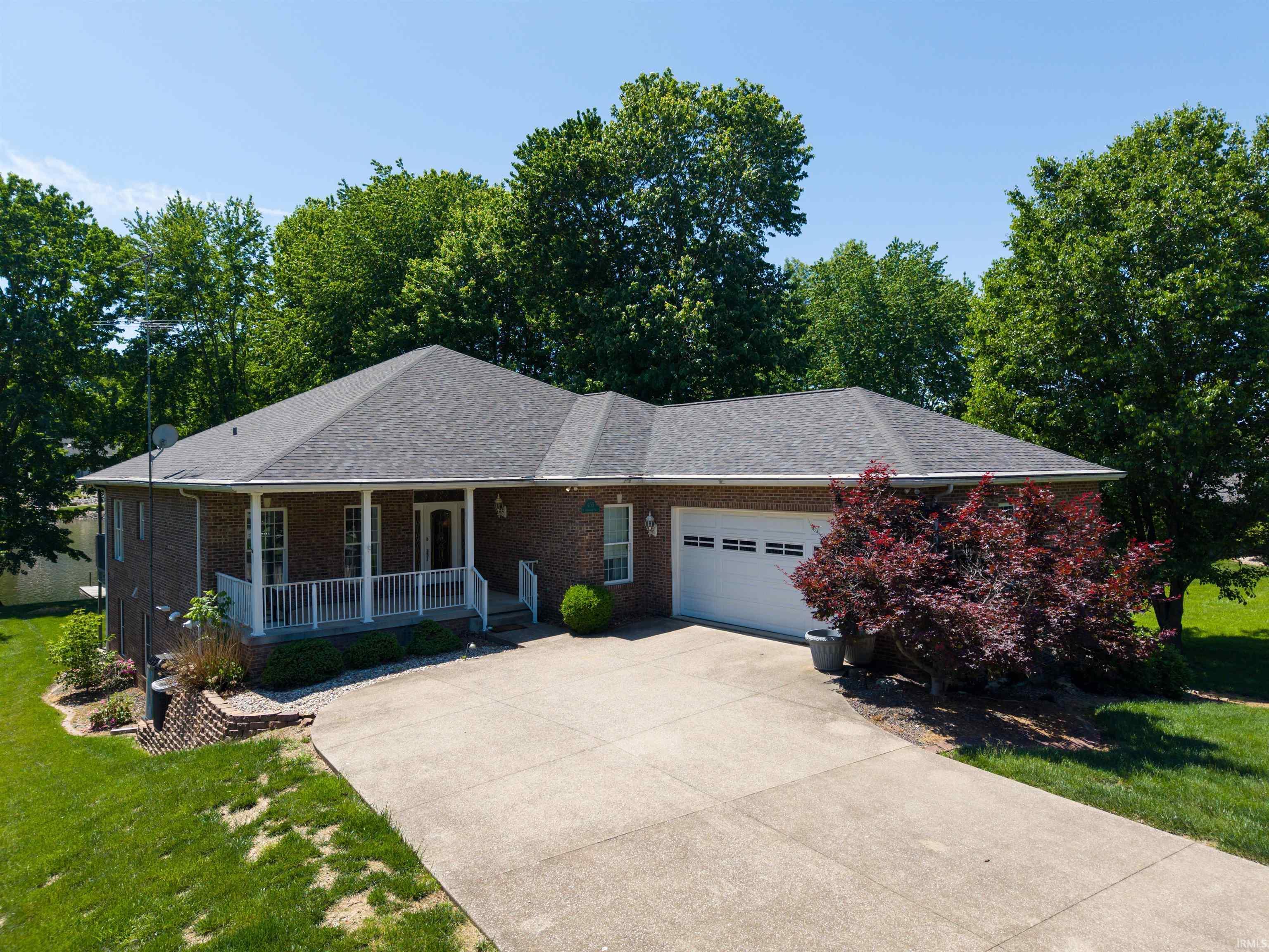 Image 2: Brick exterior featuring a covered front porch with white railings, an attached two-car garage, mature landscaping, and a concrete driveway, Front Of Structure